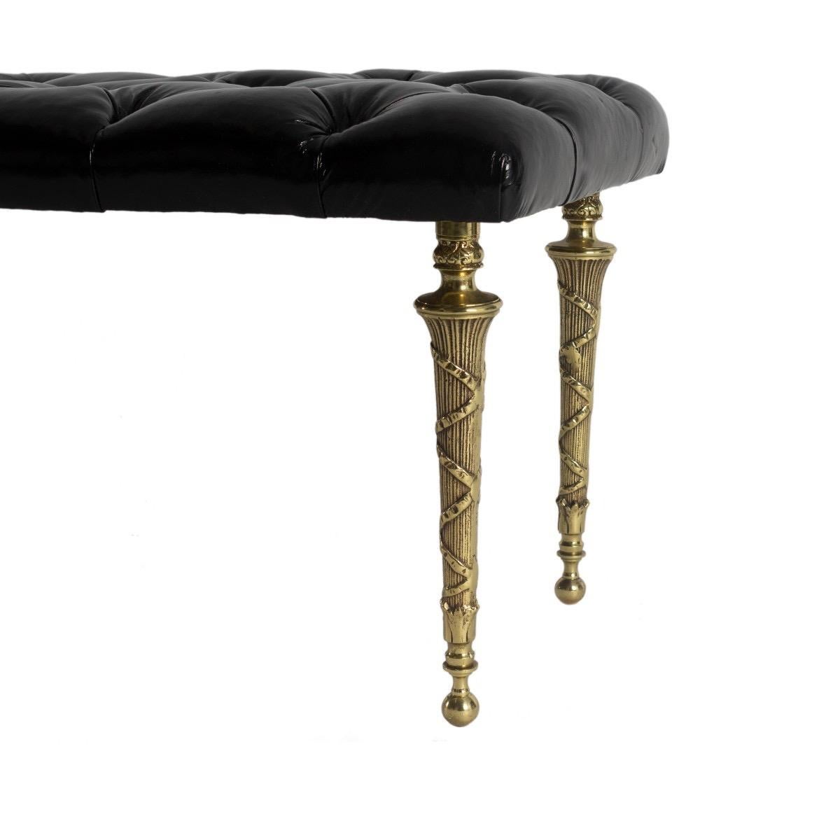 A black patent leather upholstered bench it diamond tufted seat and self-buttons, resting on six dark brass legs with ribbon detailing and ball feet, circa 2010.

Dimensions: 60