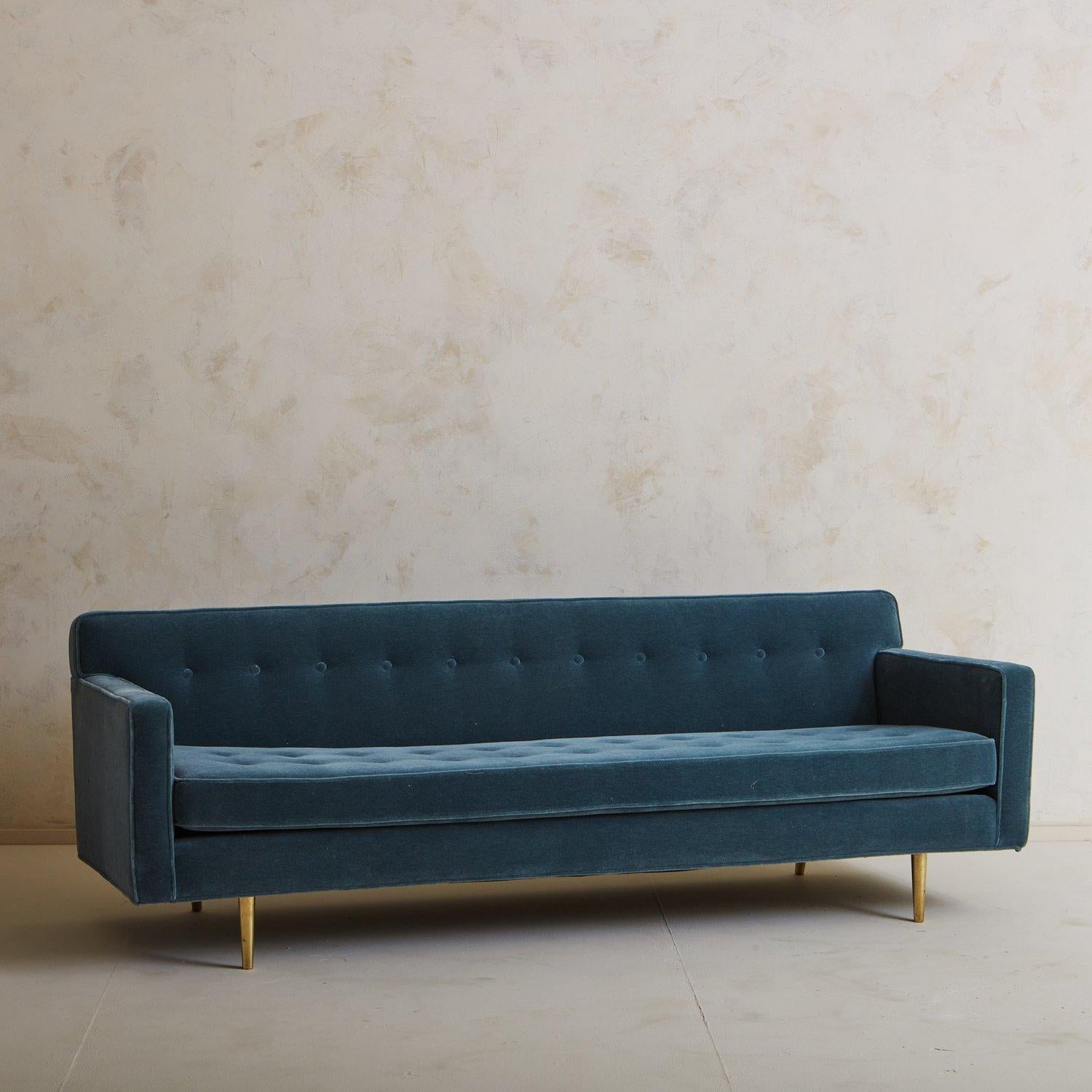 A Mid Century sofa attributed to Edward Wormley for Dunbar in the 1950s. This piece was reupholstered by previous owners in a beautiful blue mohair and features tufting details on the seat and back. It stands on four tapered brass legs and has a
