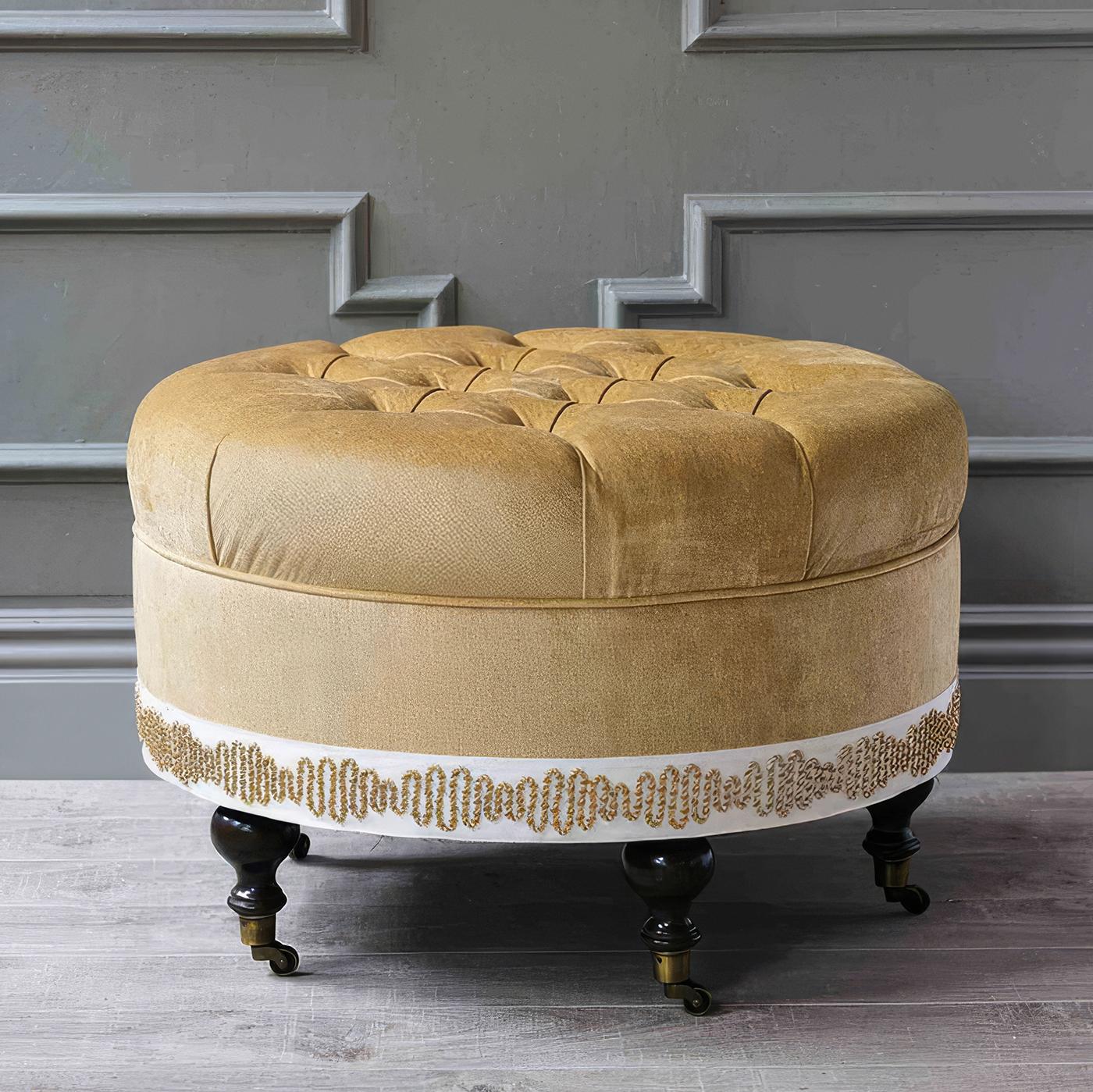 Recouvert d'un somptueux tissu de velours doré, cet ottoman glamour est doté d'un capitonnage exquis et d'une garniture décorative autour de la base, ajoutant une touche raffinée à tout espace. Fabriqué aux États-Unis par des maîtres tapissiers, ce
