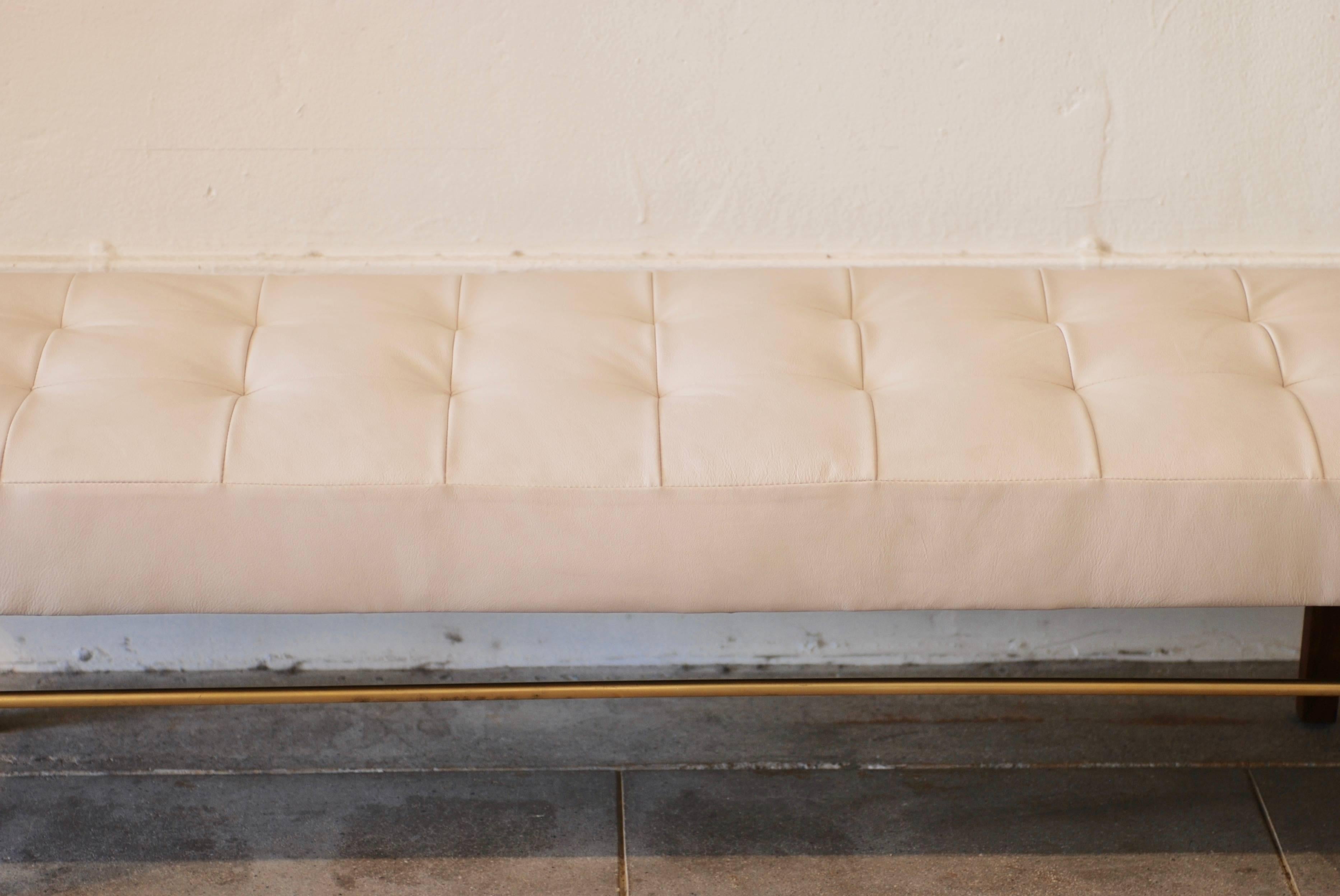 A newly upholstered tufted white leather bench with walnut and brass base.
