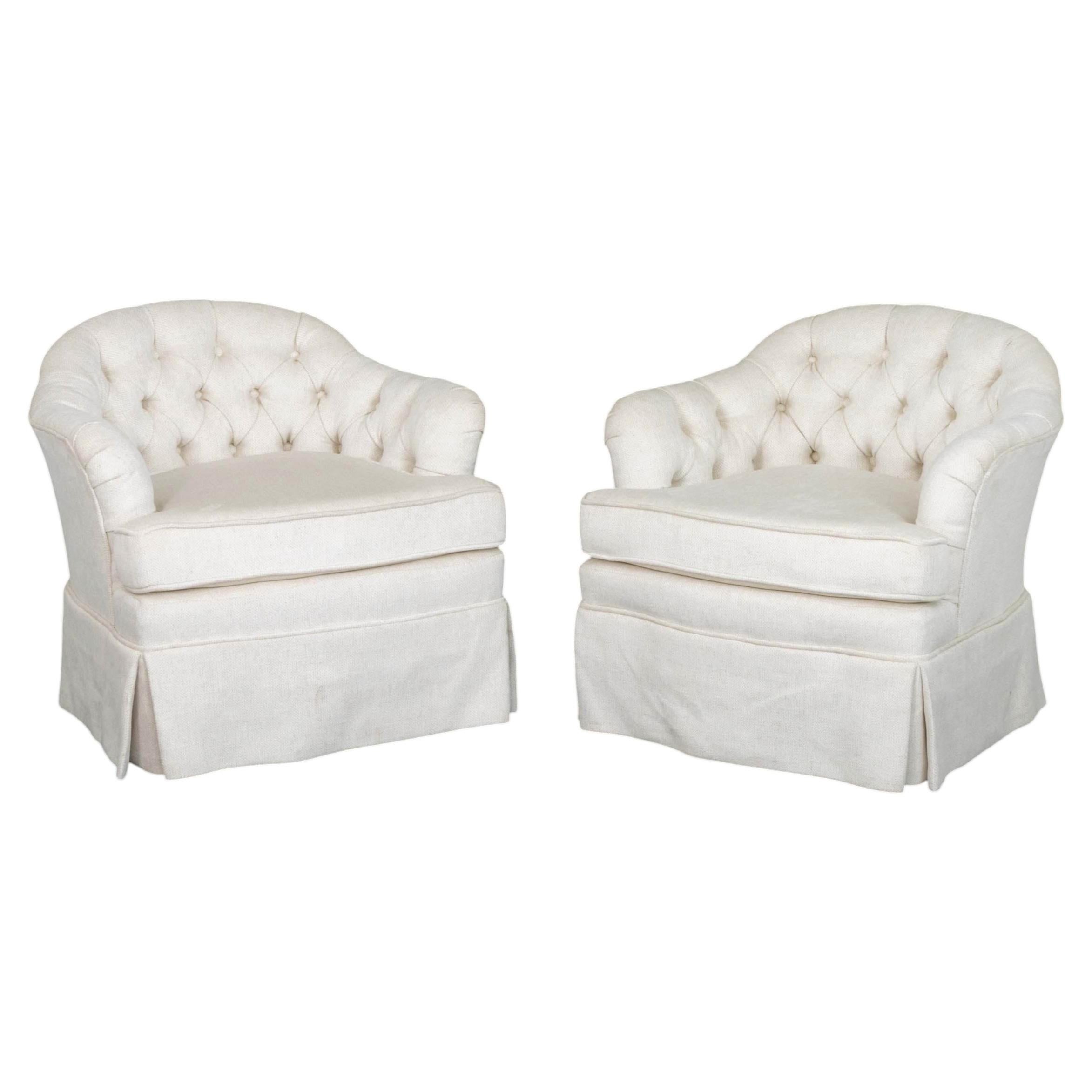 Paire de fauteuils pivotants à dossier bombé, rembourrés de tissu blanc et capitonnés de boutons.
