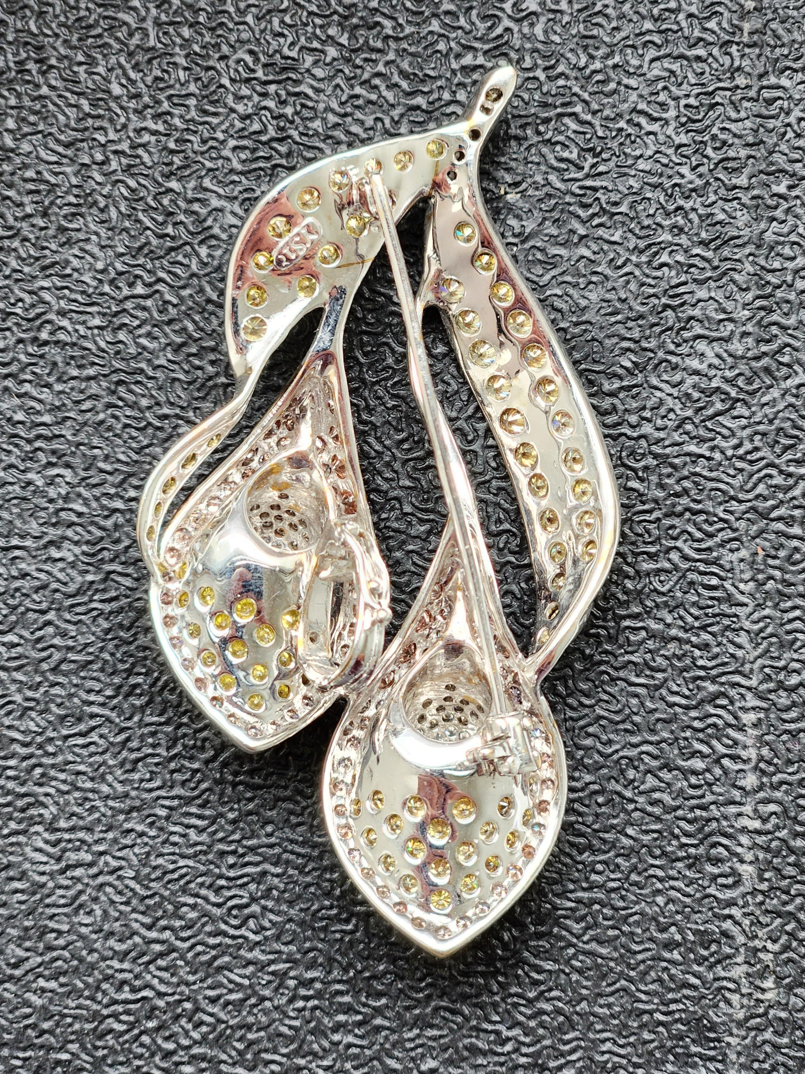 The Tulip Shaped Multicolor Diamond Brooch Pendant is a stunning piece of jewelry that boasts exquisite artistry and craftsmanship. This beautiful brooch pendant features a centerpiece of white melee diamonds surrounded by yellow melee diamonds in
