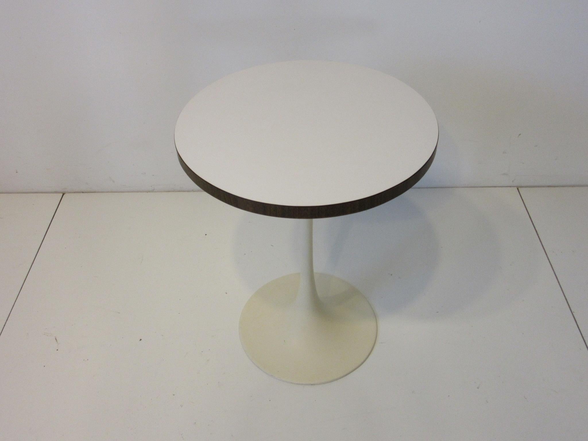 A smaller sized tulip side table with darker faux wood to the edge and cream white laminate top and cast metal base in the style of Eero Saarinen and Knoll. Manufactured by the Burke Furniture company and designed by Maurice Burke.