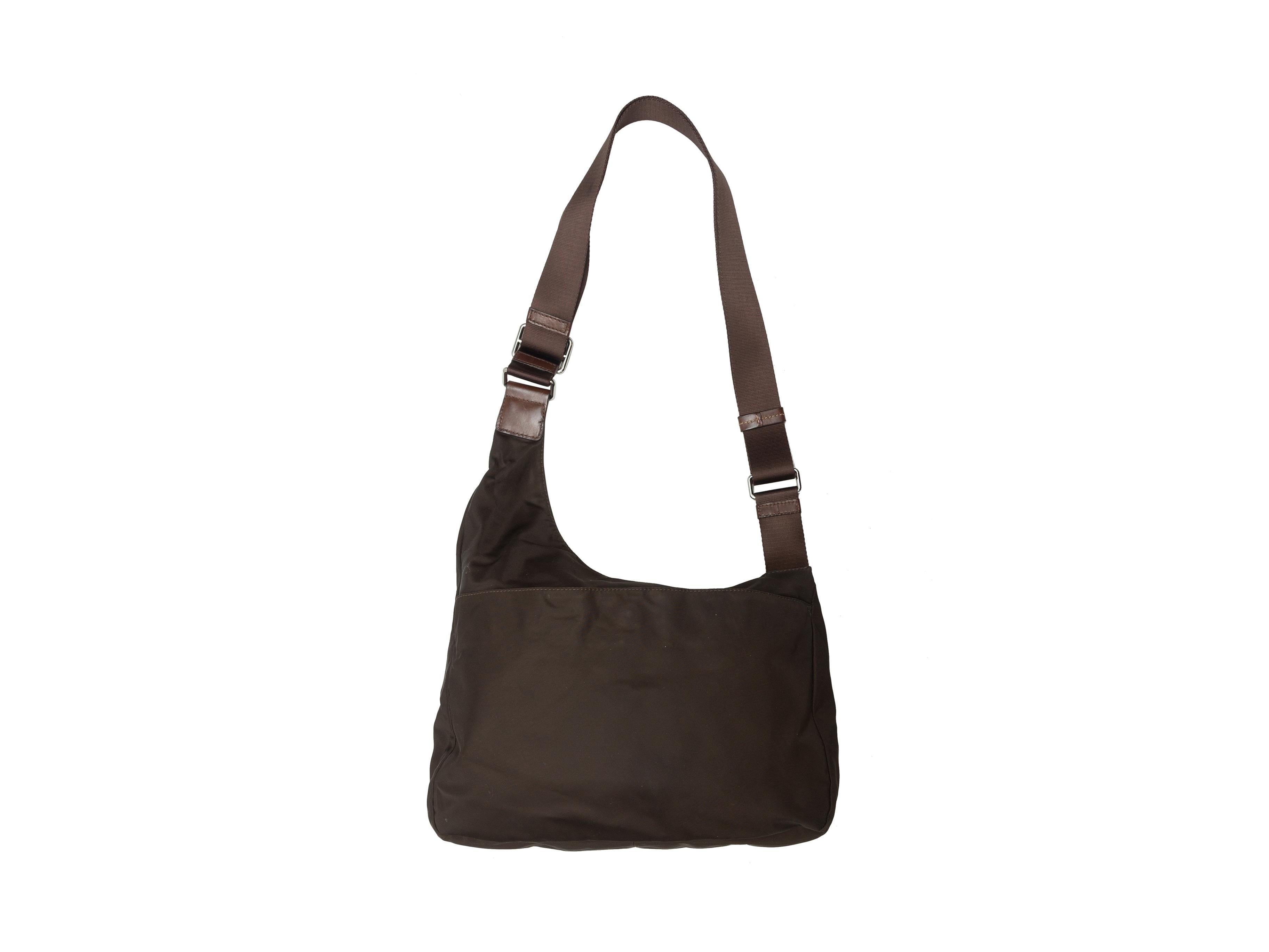 Product details: Brown nylon shoulder bag by Tumi. Silver-tone hardware. Leather trim throughout. Flap and zip pockets at exterior front. 13