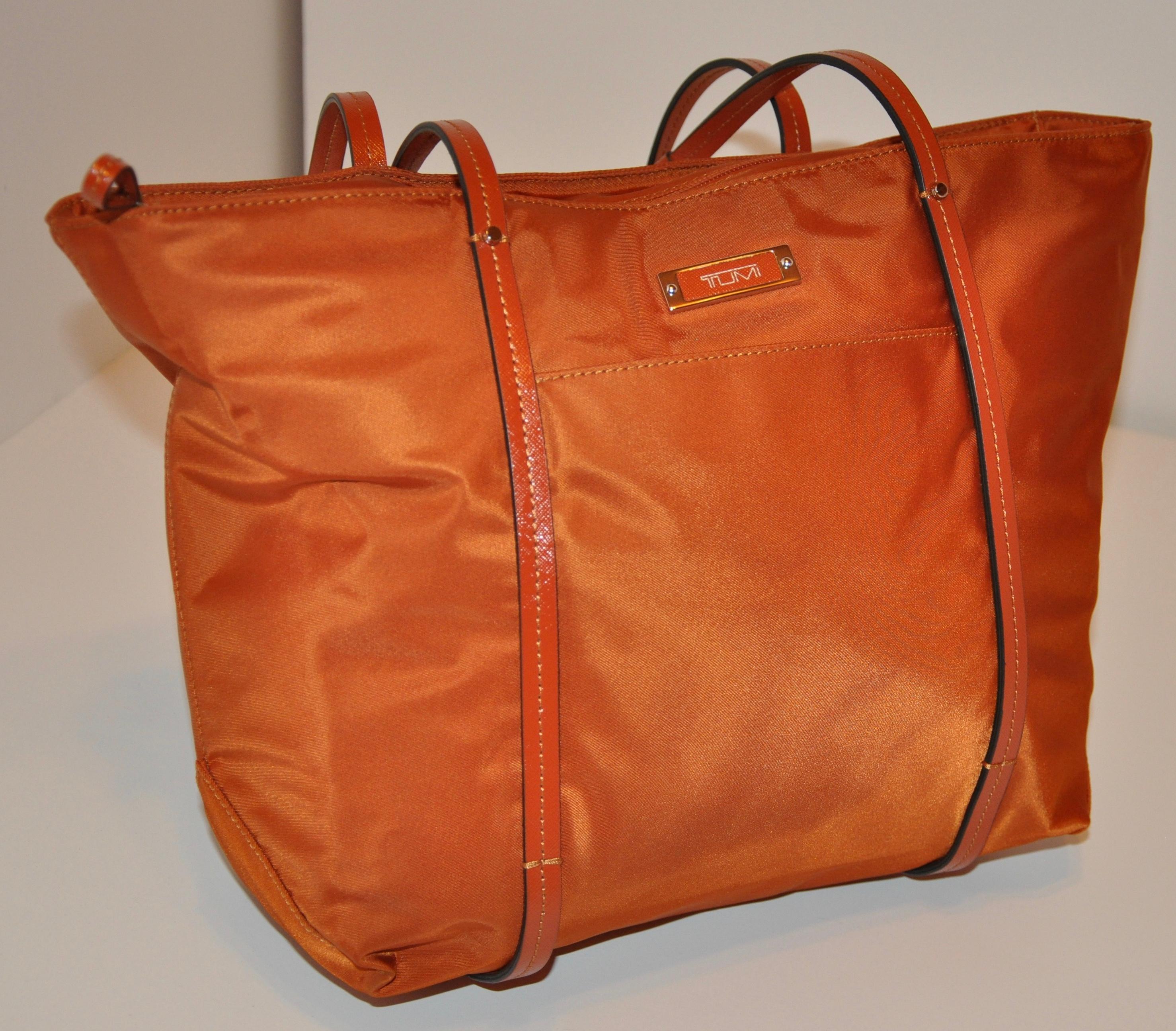        Tumi wonderfully detailed golden bronze-Tangerine nylon zippered top double-handle tote bag has a large zipper compartment as well as two open compartments within the interior for all your organizational needs when needed. The zippered top