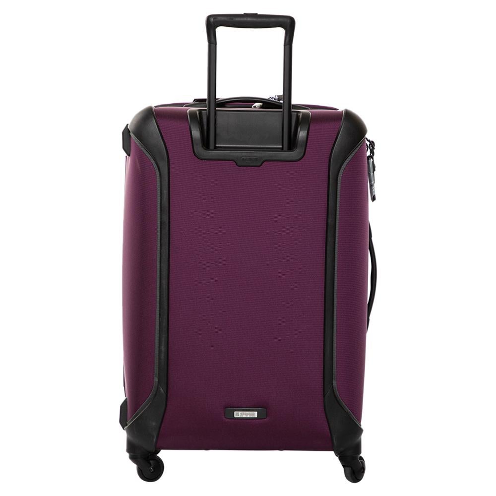 This Trip Packing Case Luggage bag from TUMI is made from purple nylon. Equipped with four wheels that offer unrestrained movement, the bag has a top carry handle along with zippers to ensure security. It boasts a nylon-lined spacious interior that