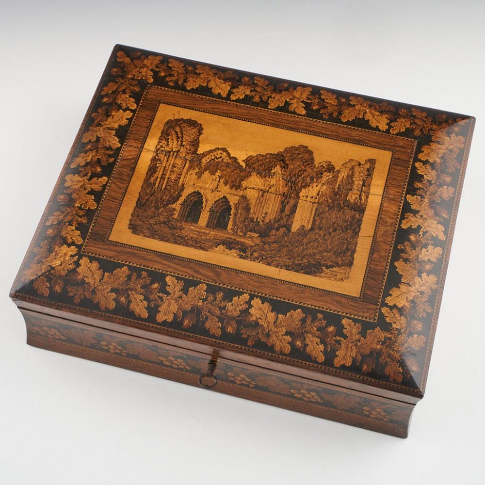 Heading : Tunbridge ware games box depicting Bayham Abbey
Date : c1865
Period : Victoria
Origin : Tunbridge Wells, Kent
Decoration : Central mosaic image of the ruins of Bayham Abbey within keylines; this is bordered by a berlin woolwork oak leaf