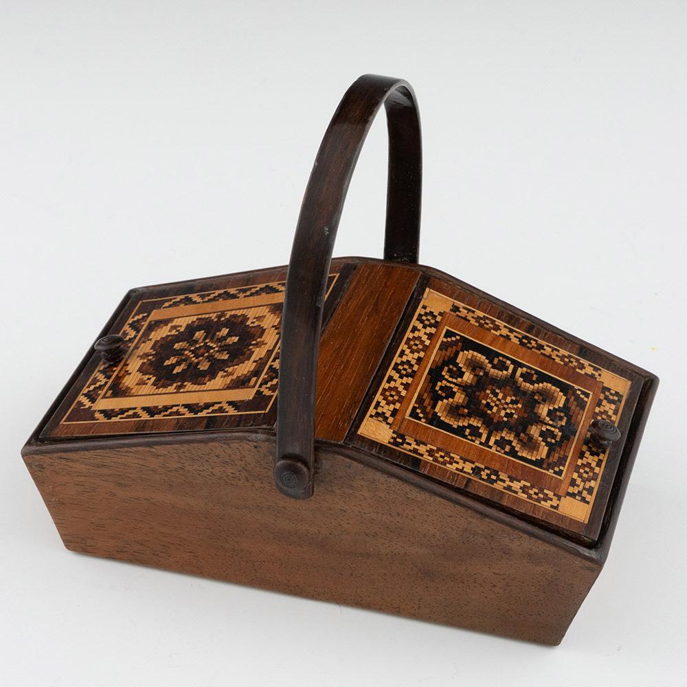 Heading : Tunbridge ware sewing box with swing handle by George Wise Jr

Date : c1865

Period : Victoria

Origin : Tonbridge, Kent

Decoration : Two sloped compartments with stylised floral mosaic within a geometric tessellated border. Swing handle.