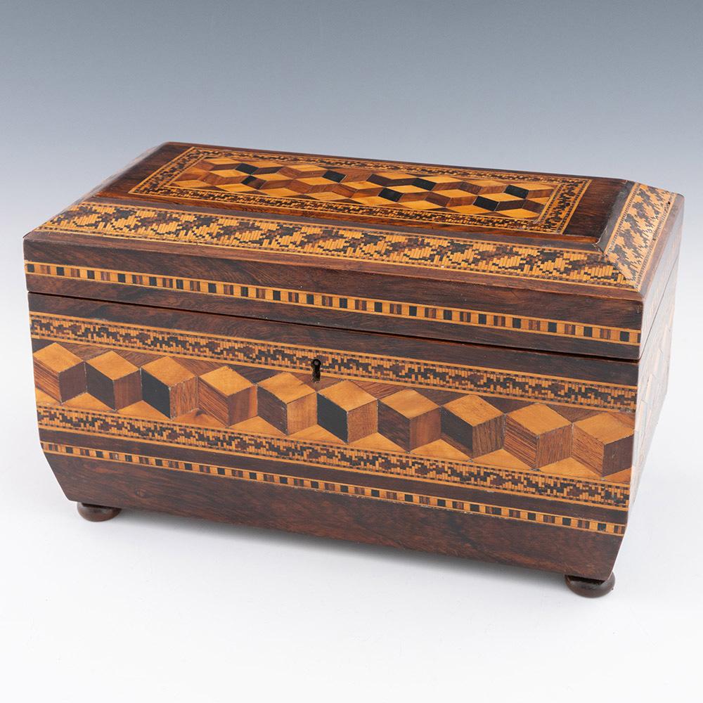 Titolo : Porta tè in Tunbridge Ware con ciotola di William Upton, 1860 ca.

Data: c1860

Periodo : Vittoria

Origine : Brighton, East Sussex

Decorazione: cubo centrale prospettico con bordo foliato. Coperchio con fascia fogliare sul bordo. Pannelli