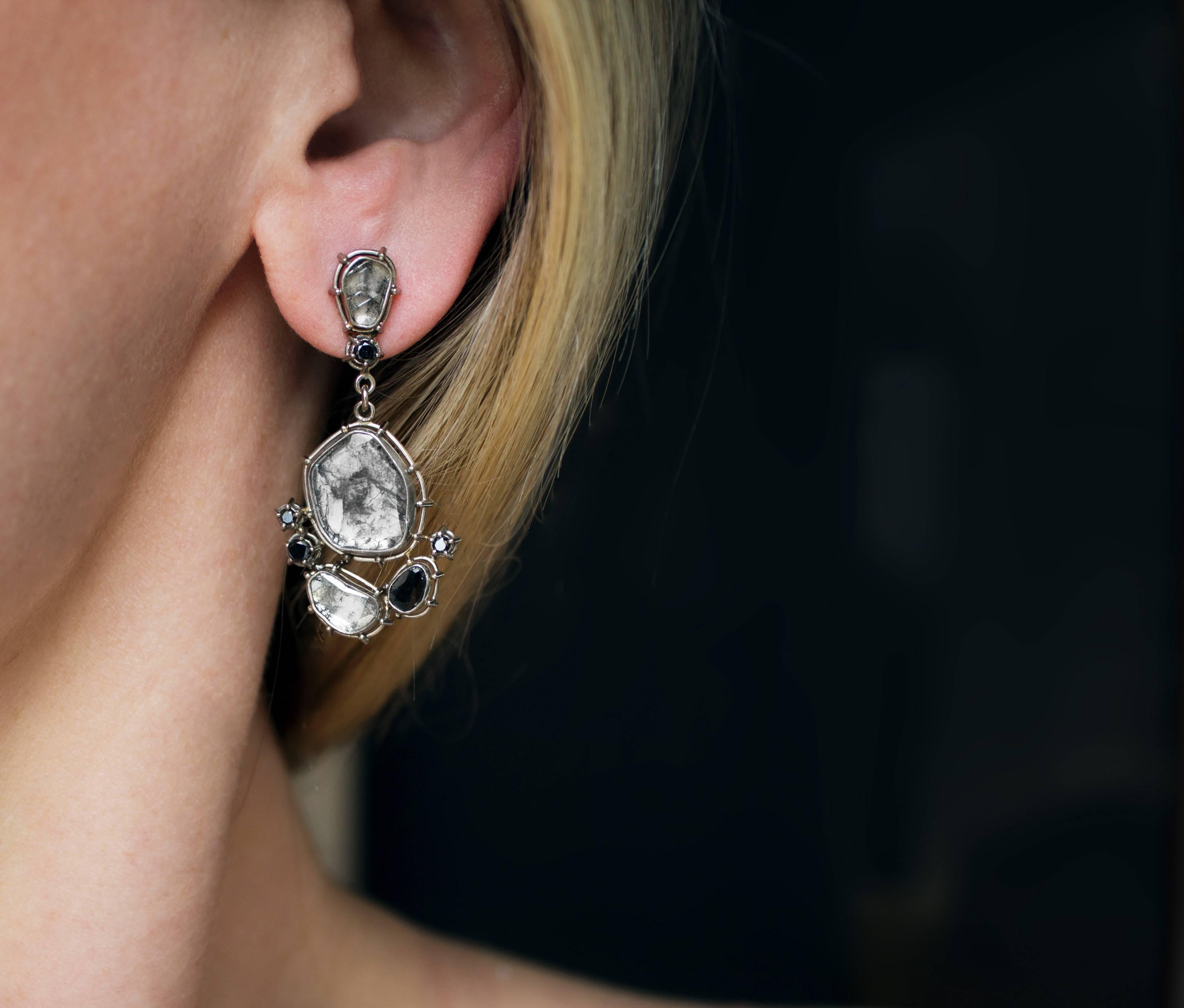 One of a Kind Dangle Earrings by jewelry artist Tura Sugden intricately hand-fabricated in 18k white gold-palladium showcasing an assortment of shimmering faceted diamonds, all bezel-set in the designer's signature raised frame settings. Stamped and