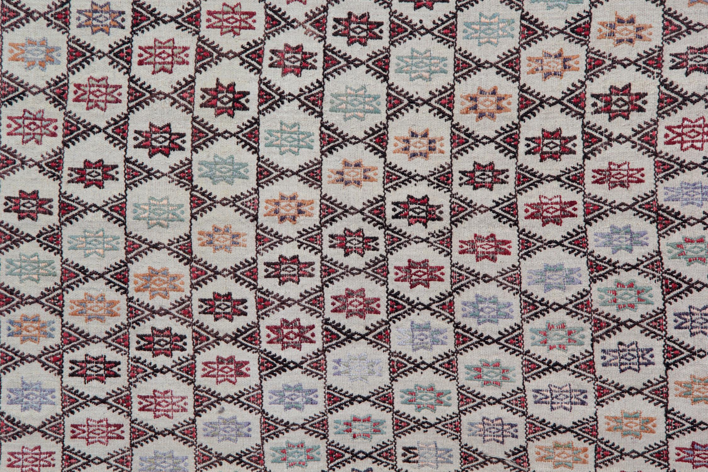 Questo antico tappeto turco Cicim Jajim Kilim del 1910 è un raro e dettagliatissimo esempio di tessitura tradizionale anatolica, caratterizzato da un'intricata disposizione all-over di motivi tribali a stella, motivi a diamante e morbide geometrie a