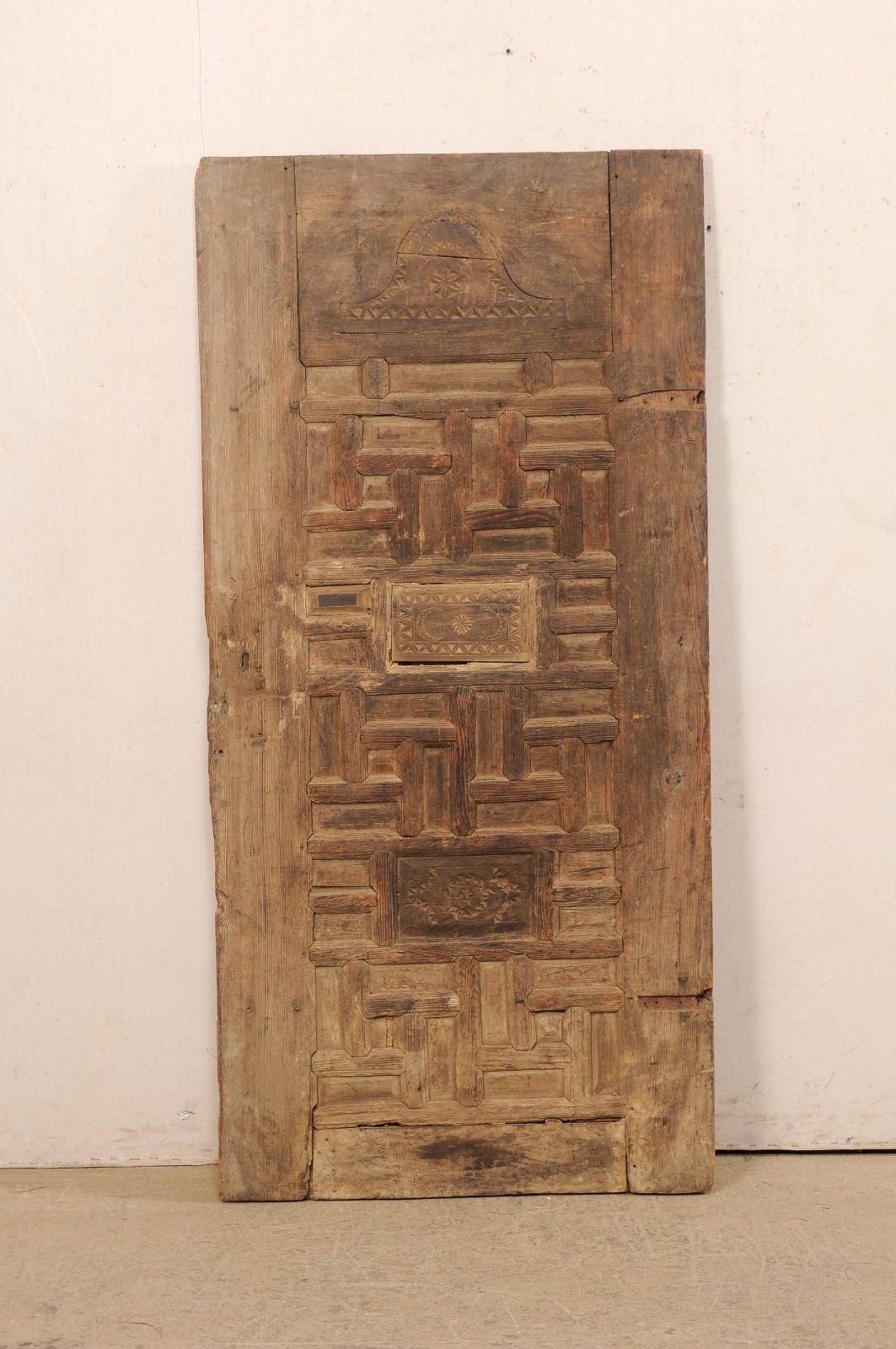 A single Turkish decoratively carved wooden door from the 19th century. This antique door from Turkey has a rustically decorated front side which has been ornately adorn in a carved geometric design, with a larger and two smaller panels that have