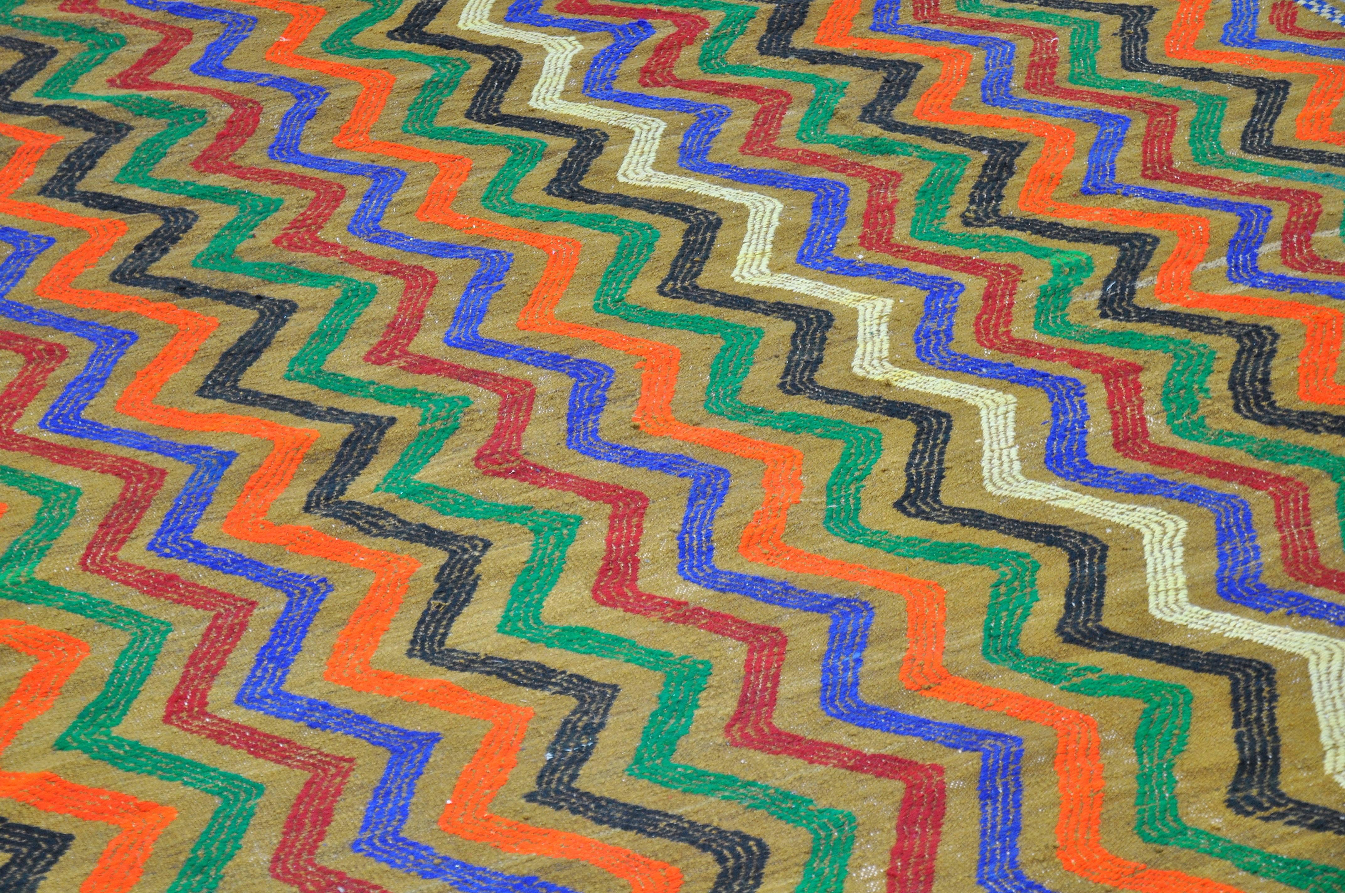 A large and thick vintage Kilim hand-knotted wool rug with vibrant red, orange, blue, green and cream zig zag patterns and tribal motifs on a light olive green background. Made with hand-spun wool and natural dyes. Works very well with Danish,
