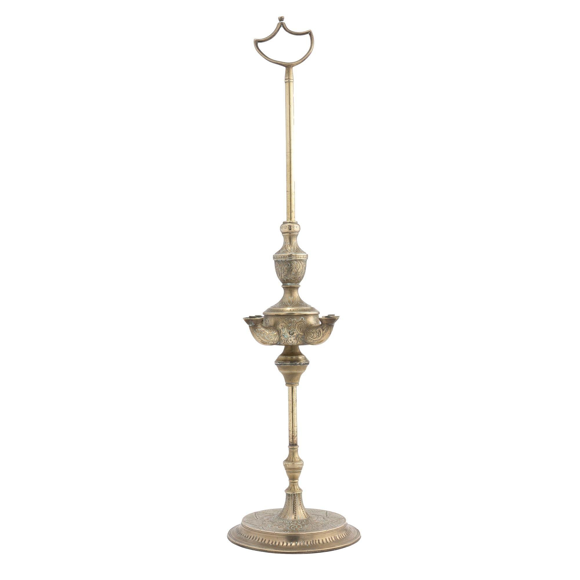 Lampada a petrolio turca in ottone fuso con fonte a quattro becchi e montata su un'asta in ottone con base circolare e un terminale a forma di scudo aperto. Il carattere scorre lungo l'asta con il supporto di un rocchetto di ottone indipendente con