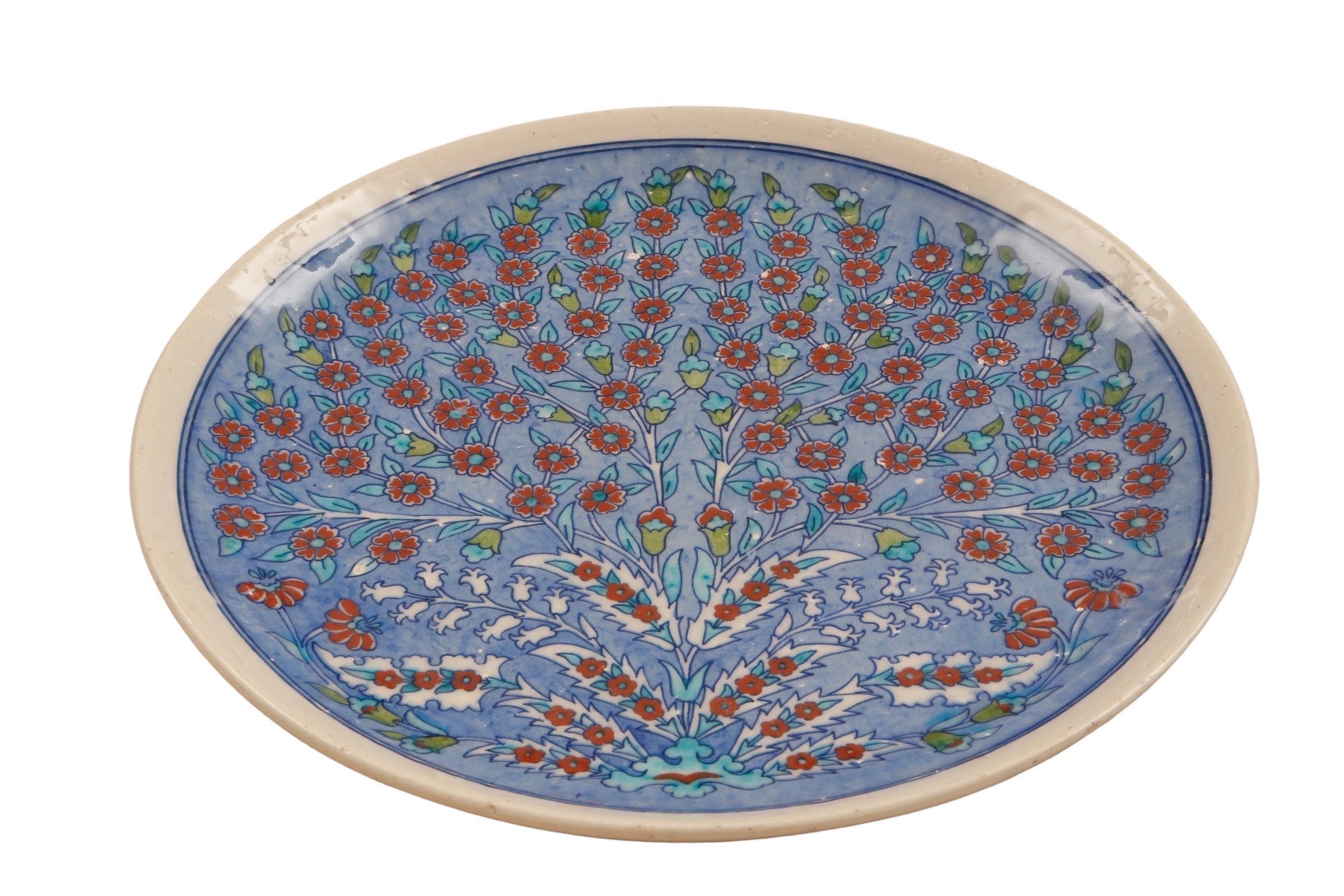 Assiette ou plat turc fabriqué à la main, décoré d'un motif classique d'Iznik datant de 1550. En céramique, avec une glaçure polychrome, le plat aplati est peint en bleu cobalt aqueux. Un arbre de vie central s'épanouit avec des rosettes rouges,