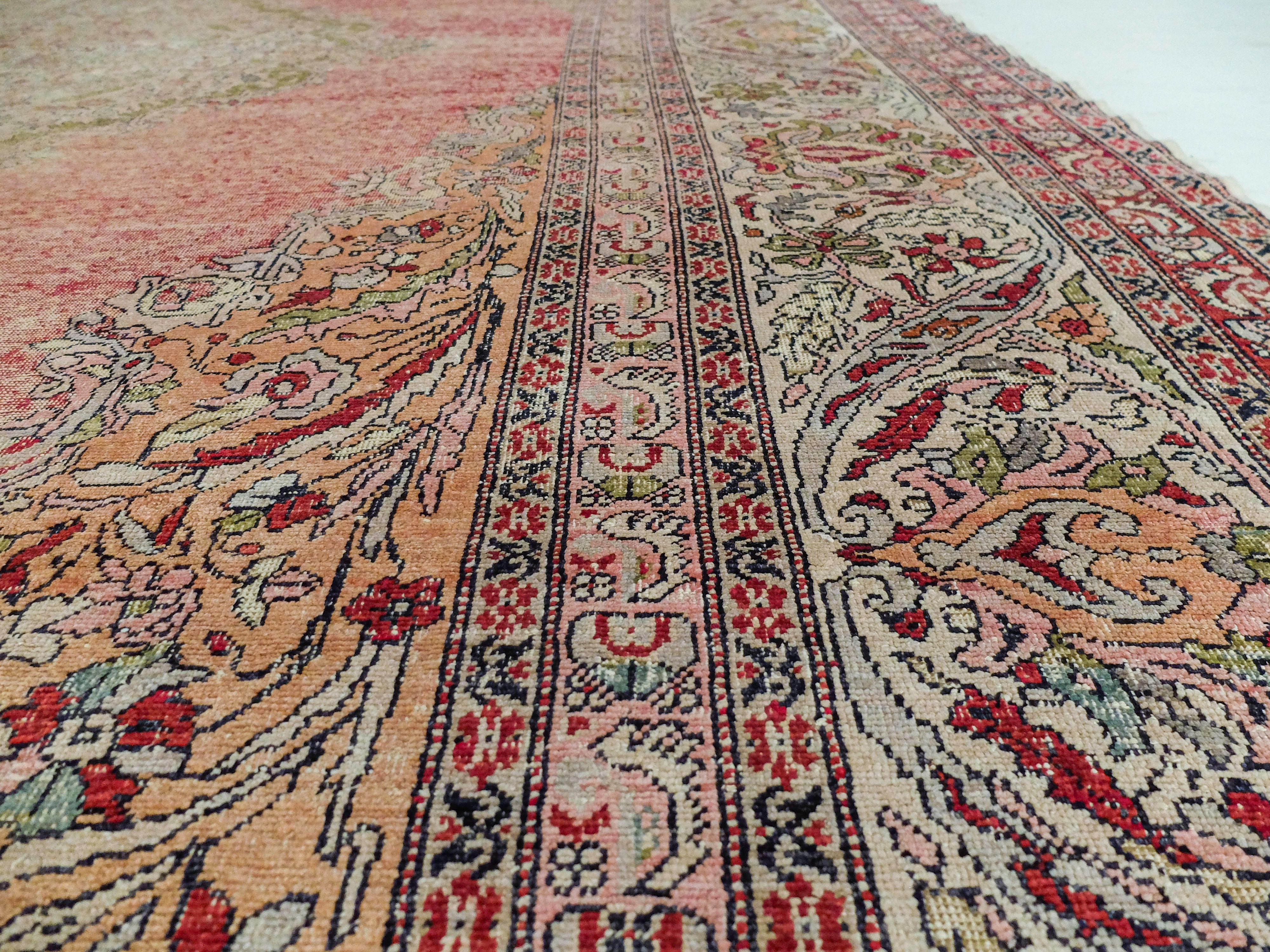 This Turkish Kayseri rug was made c. 1880s. It has a large intricate diamond in the middle composed of smaller floral and organic shapes. This shape is surrounded by a red field, and bordered by more floral patterns. This rug has several patterns