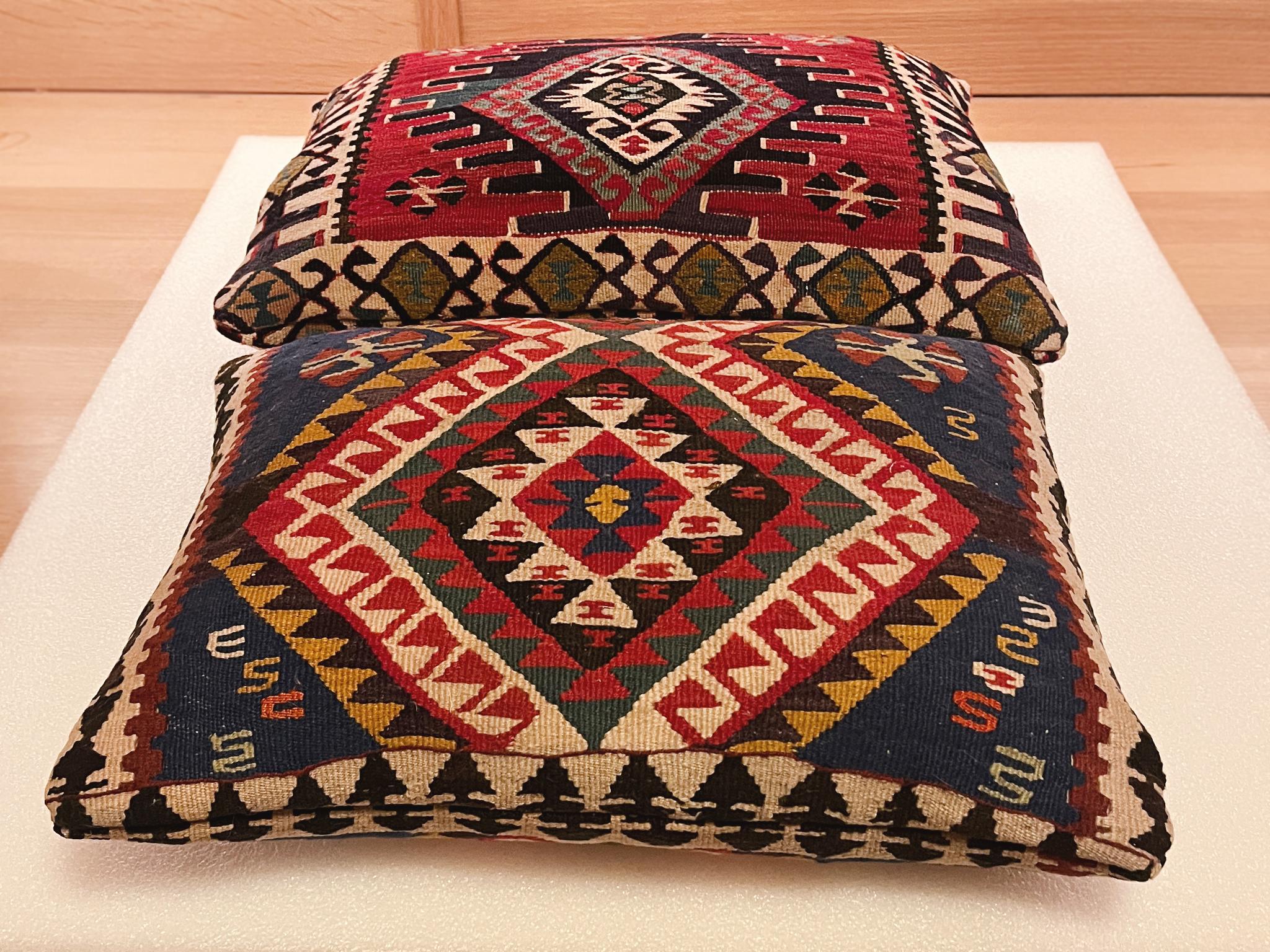 These custom pillows are made from 20th Century Turkish Kilim wool rugs. The pillows are not an exact pair but are a perfect match: each one is adorned with the Kilim rug's bold, vibrant geometric patterns in a palette of reds, greens, blues, black,