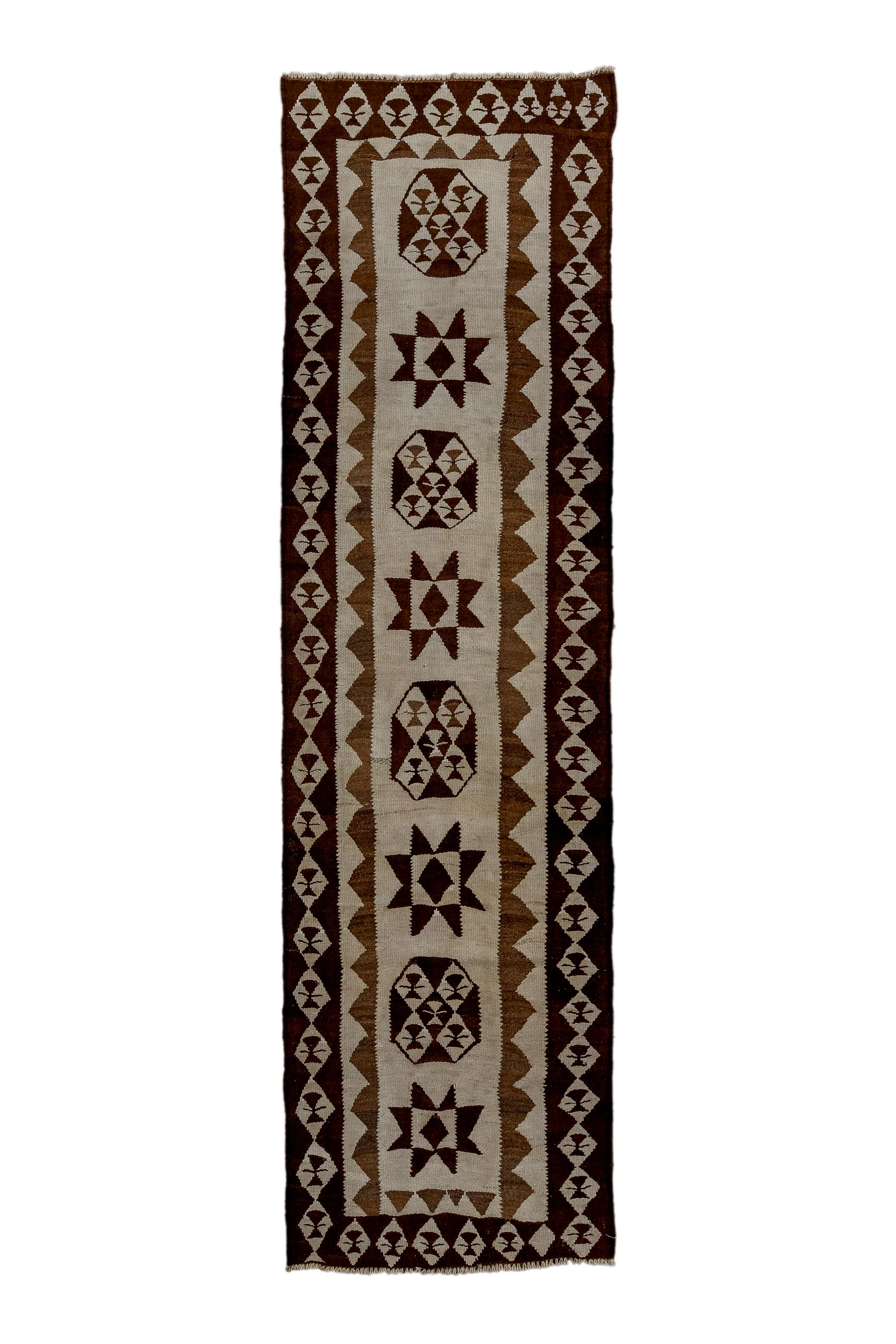 This tapestry woven flatweave has reduced the palette to ecru, darkest brown and deep red, and the design to an open field with an alternation of stars and X-centred octagons. Main border of chains of ecru diamonds and an inner triangle reciprocal