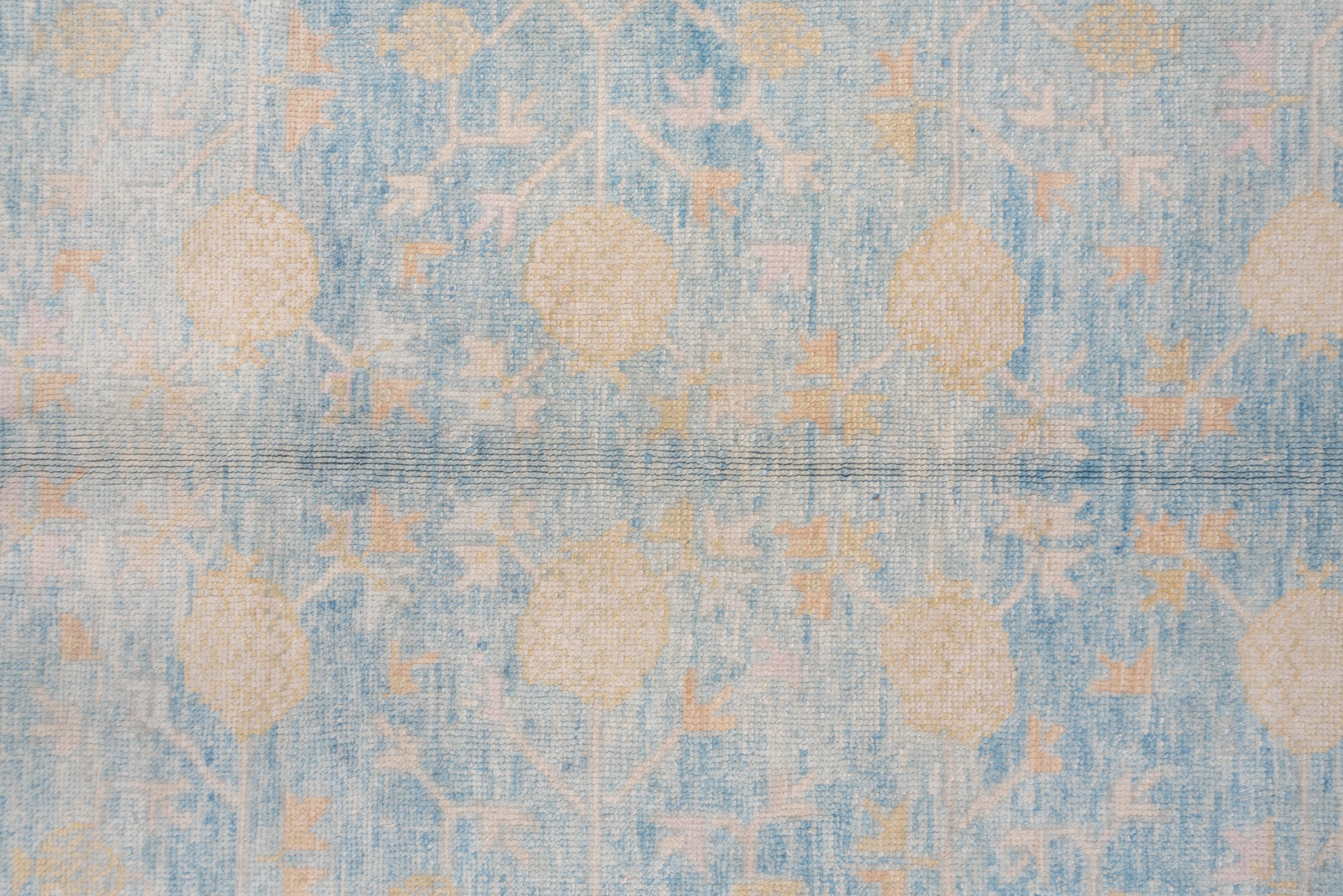 The field abrashes from powder blue to sky blue while showing an all-over elliptical palmette and open diamond design with straw details. Sand and ivory border with a floral reciprocal pattern.