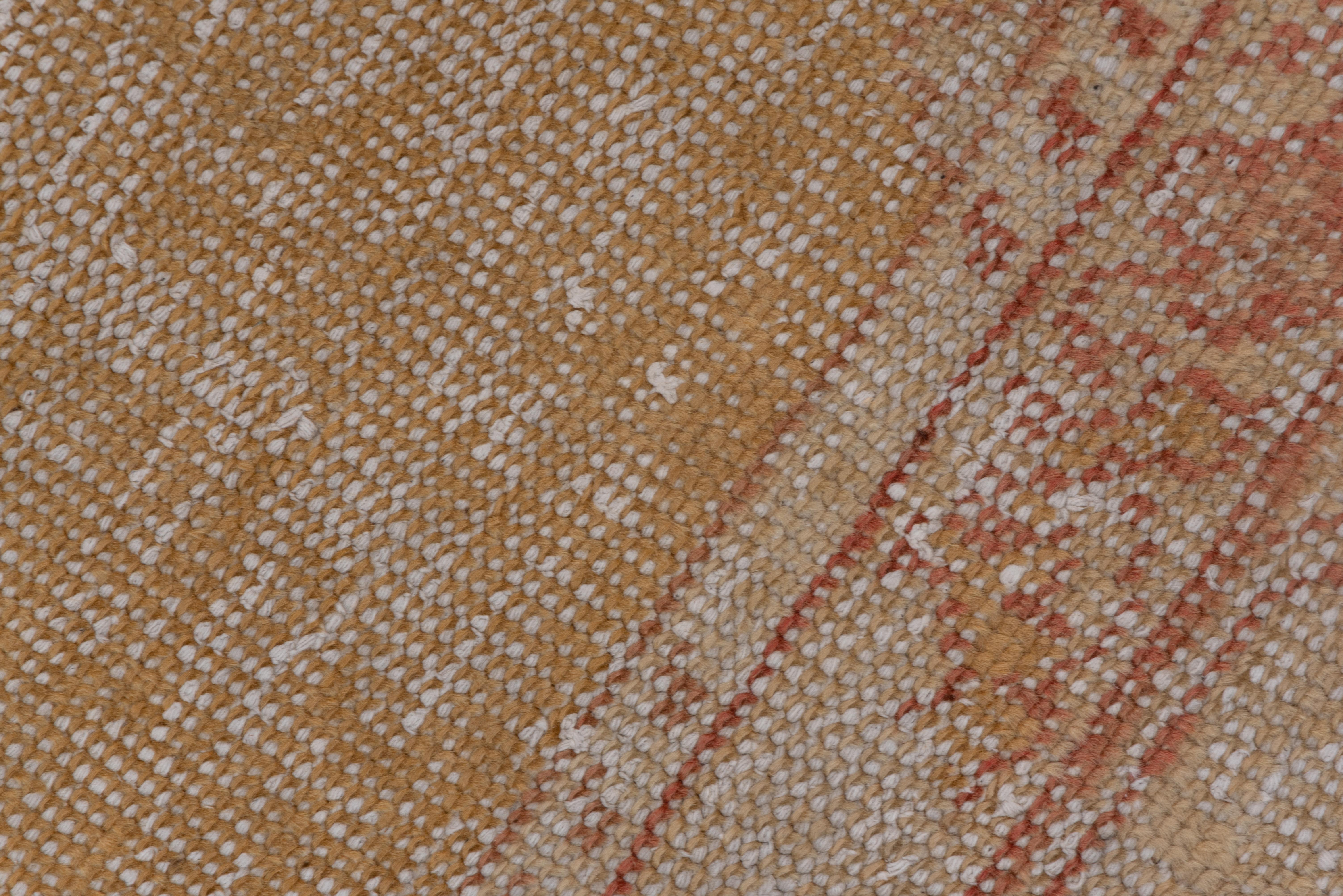 Somewhat distressed, this open, yellow field western Anatolian town carpet presents rust corners with light palmettes and thick stems. The main border alternates open cartouches with buff octofoils. Minimal design, soft colors. A big shabby chic rug.