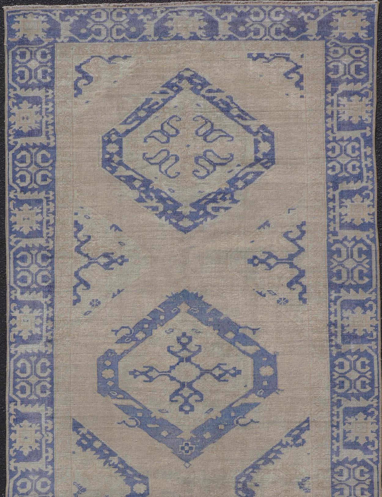 Measures: 4'6 x 12'6 

This vintage Oushak gallery runner features blue medallions on a sandy-taupe field. The border and central medallions are both rendered in a rich medium blue, as well as the border accents complimenting the field.