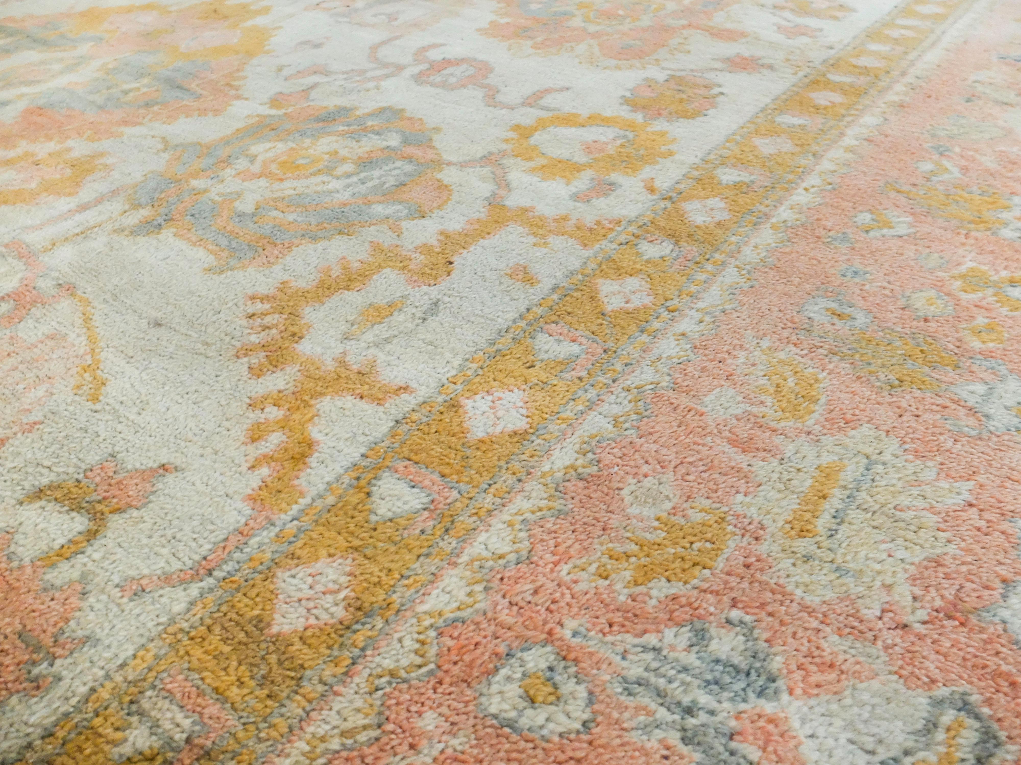 This is an Turkish Oushak rug made c. 1870s. It has a delicate soft peach, cream, and gold color way. The rugs center has large abstract floral shapes which are surrounded by 4 patterned borders. It is completed with subtle fringes at the top and