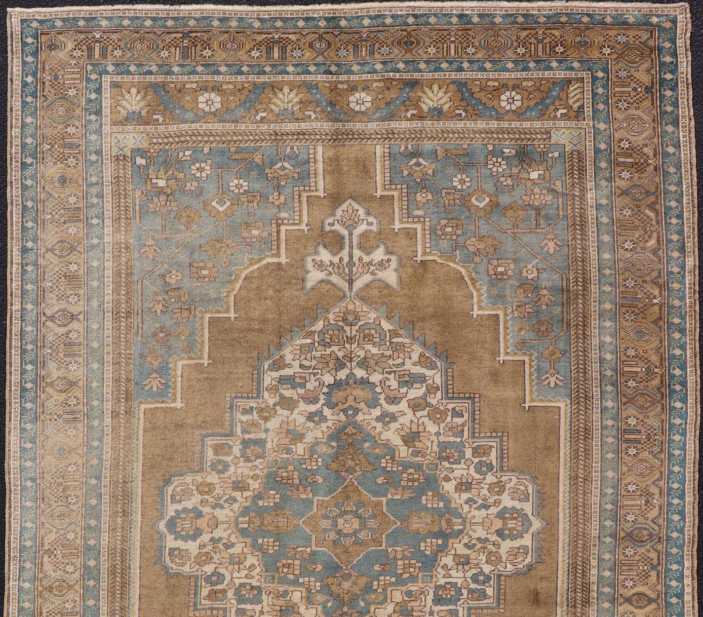 Vintage Oushak Teppich aus der Türkei in Blau- und Goldtönen, Teppich TU-NED-1029, Herkunftsland / Art: Türkei / Oushak, um 1950

Dieser türkische Oushak-Teppich im Vintage-Stil zeichnet sich durch ein kunstvoll gestaltetes Medaillon in der Mitte
