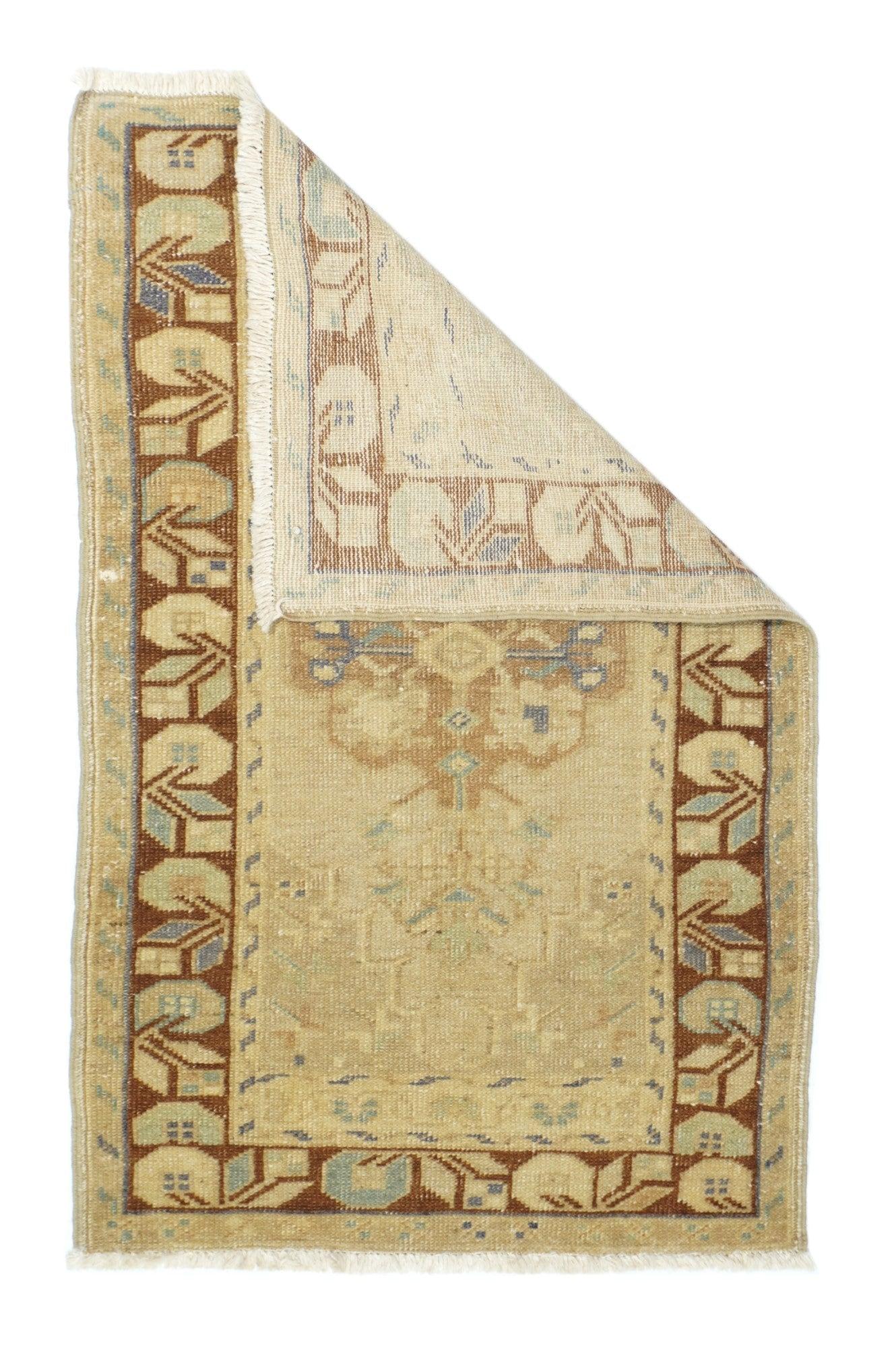 Alfombra turca 2'3'' x 3'9''. El campo, de color beige pajizo, presenta un contorno escalonado y está centrado por un medallón octilobulado, radiado de palmetas de color óxido. Borde marrón siena con módulos de flores y hojas geométricas flotantes.