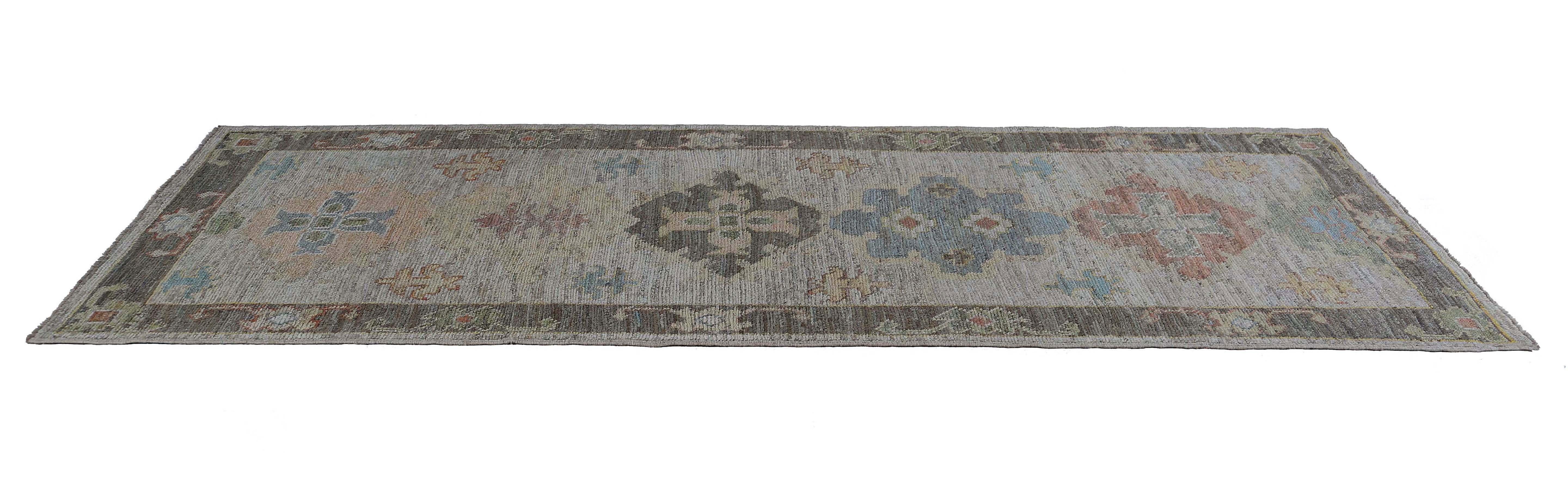 Dieser Läufer ist 3'3'' x 9'8'' groß. Dieser wunderschöne Läufer im türkischen Oushak-Design zeigt eine auffällige Anordnung von blauen, gelben und orangefarbenen Blumenmedaillons vor einem warmen braunen/grauen Hintergrund. Die filigranen