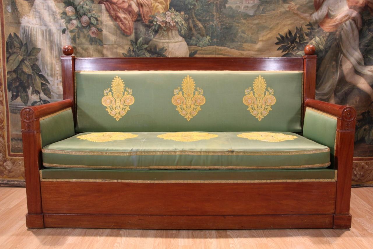 Elegant Empire period sofa, early 19th century, with a solid mahogany frame. It features a straight backrest framed by flat uprights topped with turned pommels, typical of the Empire style. The flat armrests are highlighted by small columns finished