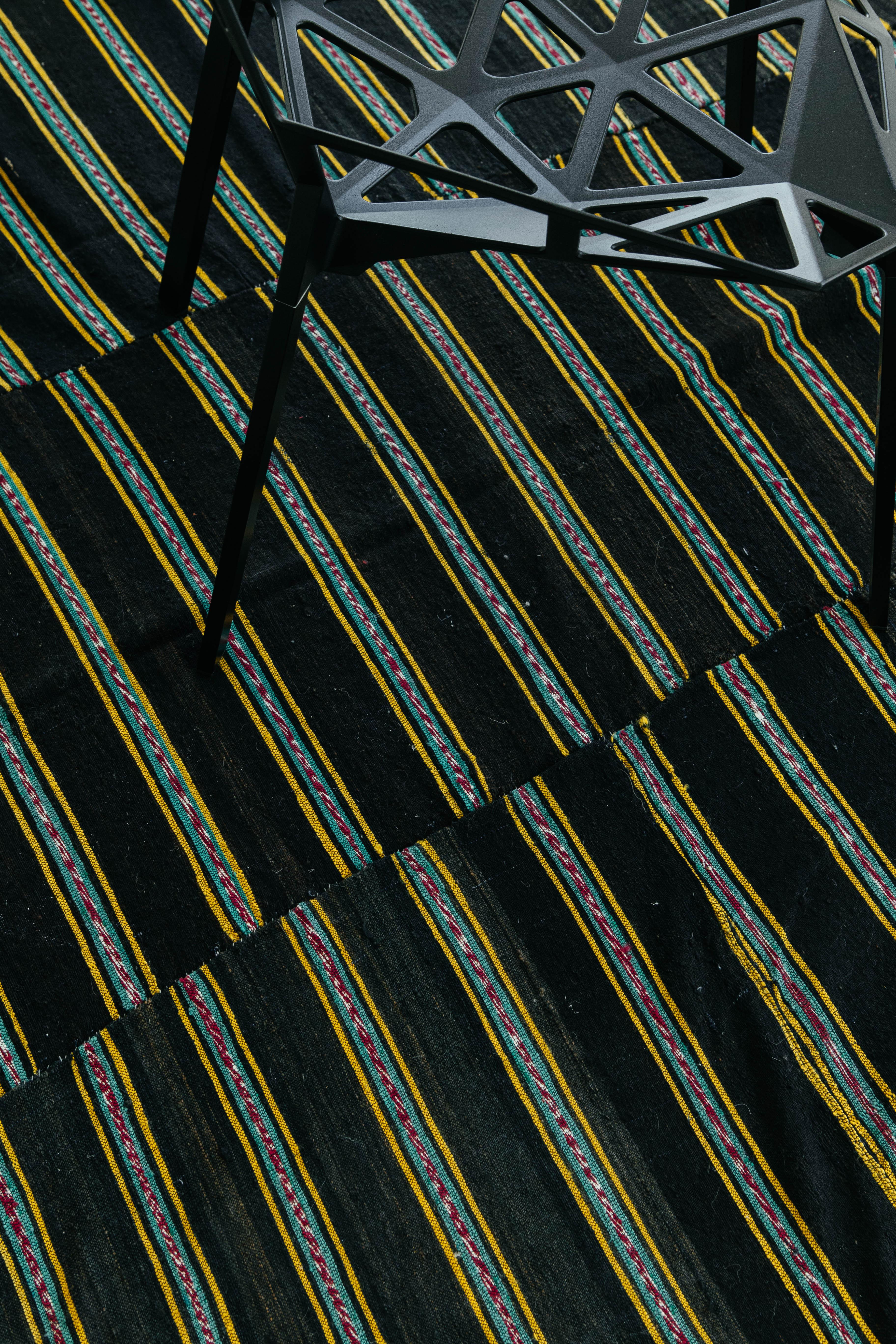 Ein türkischer Tisse-Kilim-Flachgewebe-Teppich mit einem braunen Feld und Bändern aus bunten Tribal-Streifen. Dieser Kelim hat eine vertikale Bänderung sowie unregelmäßige horizontale Linien in Gelb, Rot, Schwarz, Weiß und Grün. Dieser Teppich