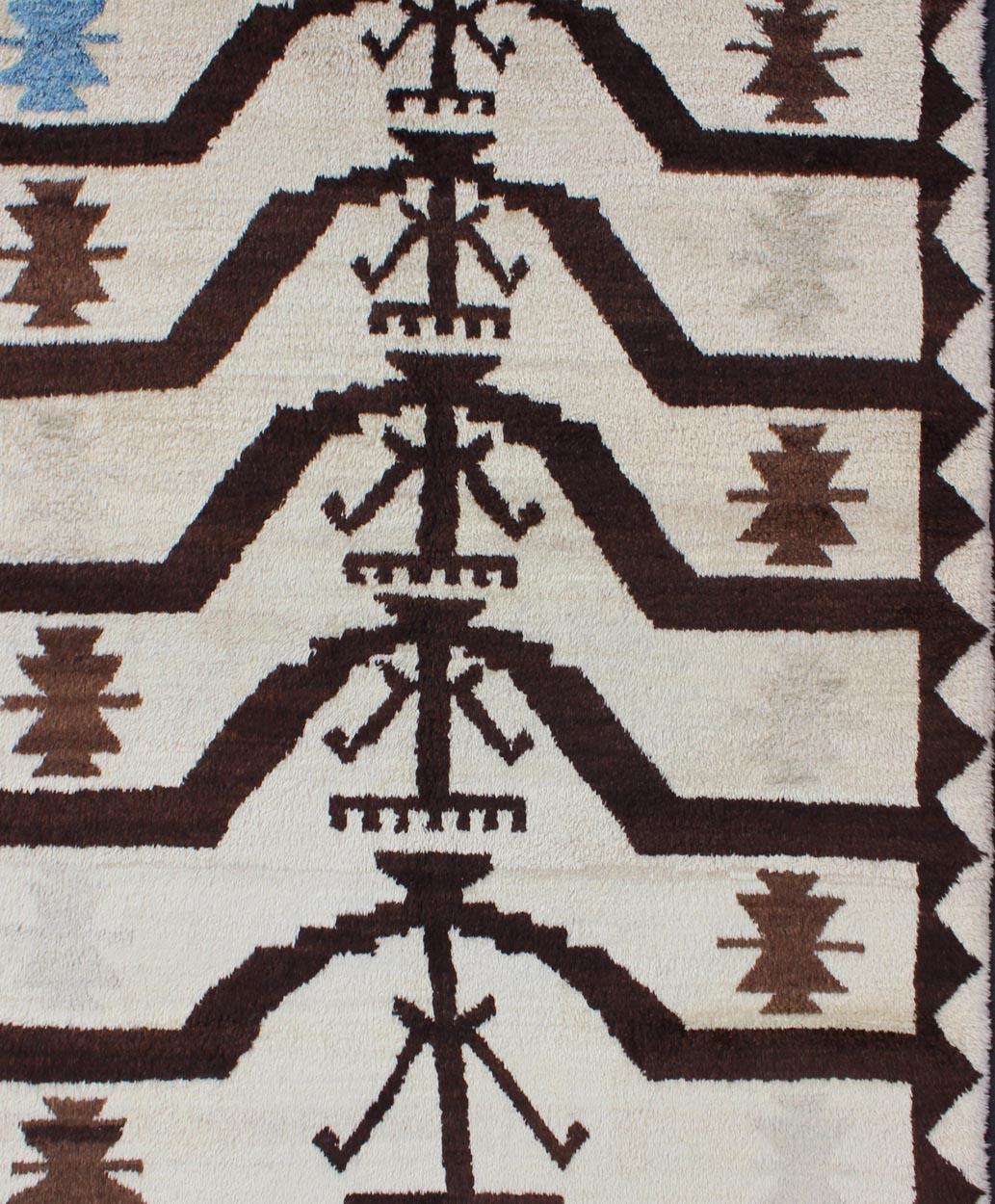 This fantastic Turkish Tulu rug features a stunning Mid-Century Modern design enclosed within a semi-checkered border. The colors included are brown, off-white and blue. The wool used in these rugs is exceptionally fine and durable, in combination