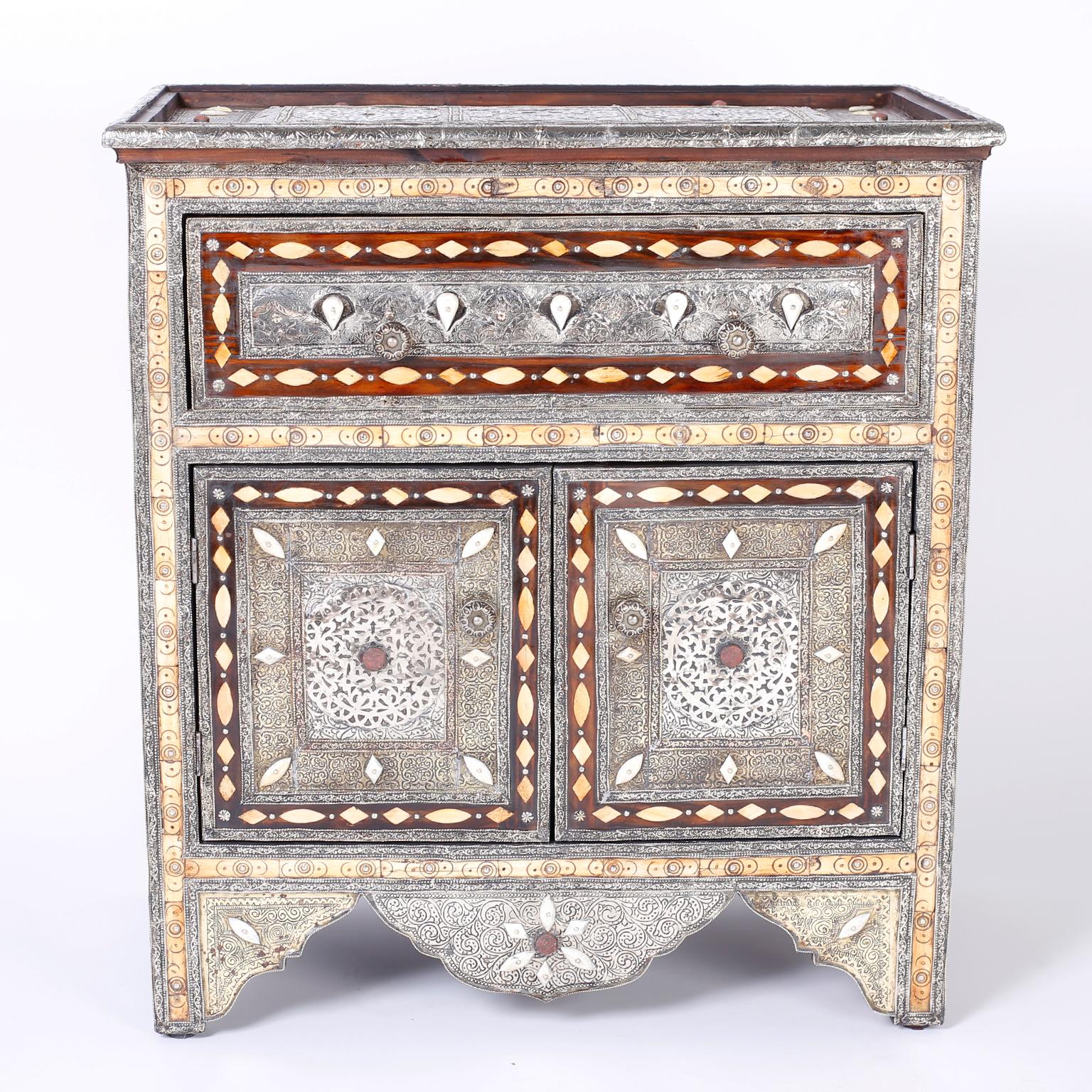 An enchanting Turkish cabinet or stand showing Syrian influences with elaborate hand-hammered floral designs on tin over a hardwood frame. Featuring semi precious stones, bone inlays, stick and ball panels and plenty of storage with a drawer and two