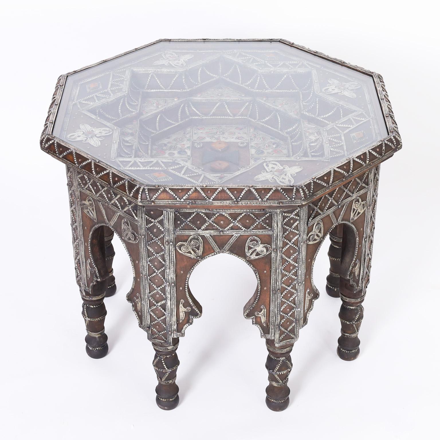 Impressive vintage Turkish stand or table crafted in indigenous hardwood in an octagon form featuring ambitious decorations of tooled jewelry like metal work, a deep step down top under glass with enamel work, dyed bone, and semiprecious stones. The