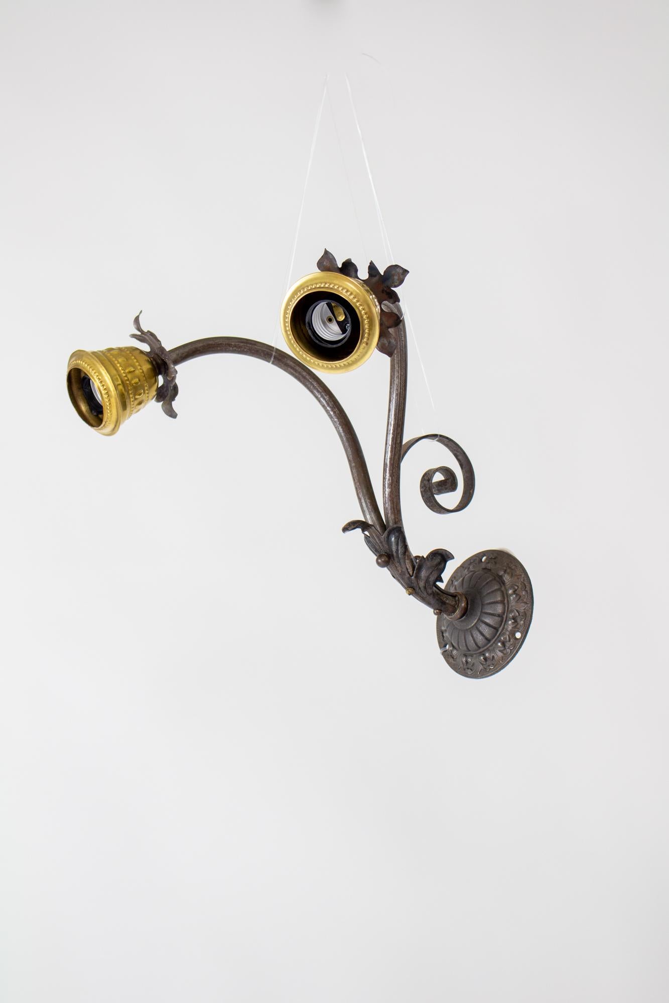 Turn of the 20th Century wrought iron and brass sconces. Cast iron backplate in a Victorian style. Iron arms with iron decorations. Decorated brass candle up provides a contrasting pop. A single arm splits into two and curves up and then down to