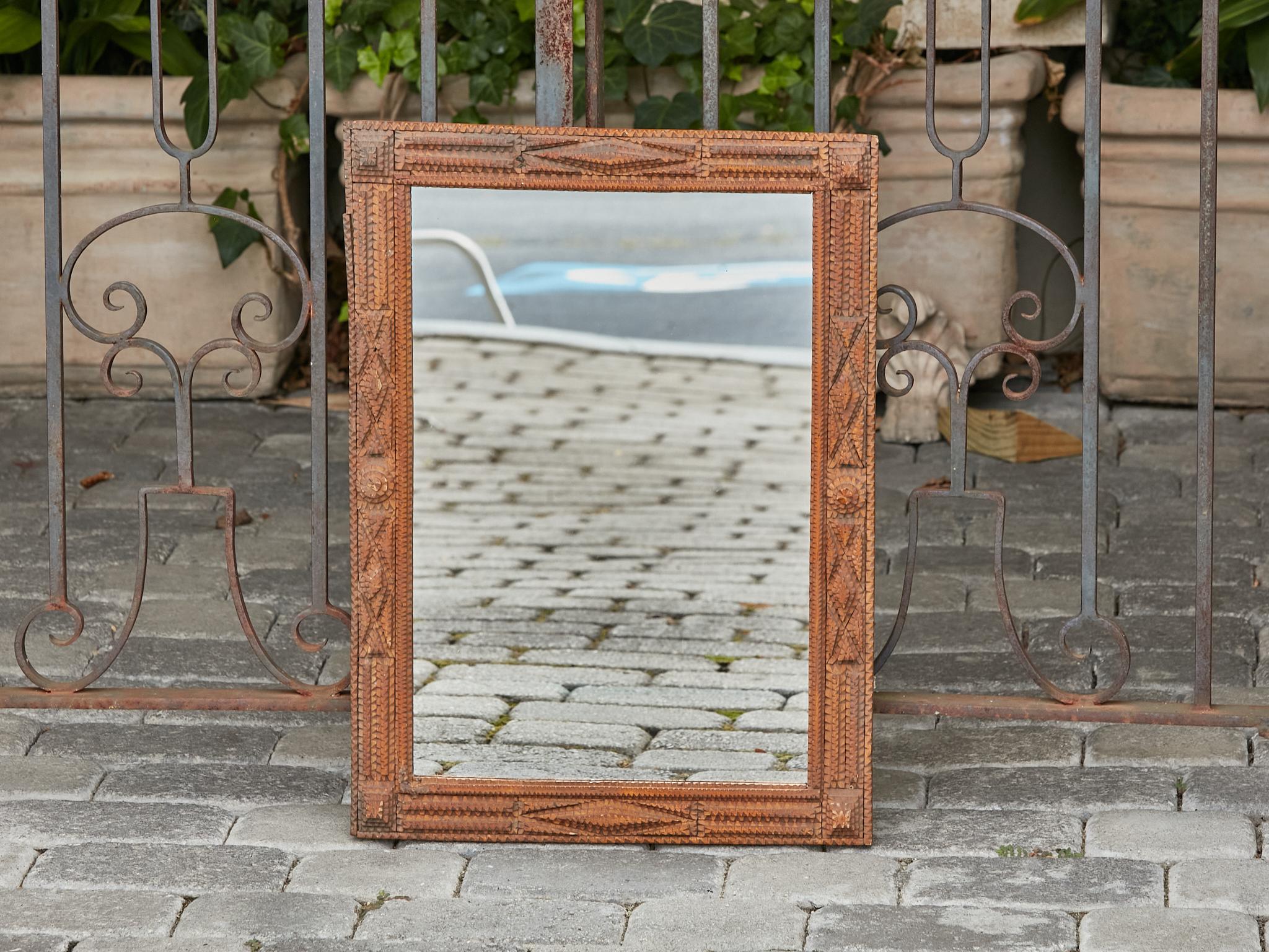 A French Tramp Art hand-carved wooden mirror from the Turn of the Century circa 1900, with raised motifs and brown patina. Step back in time and embrace the rustic charm of this exquisite French Tramp Art hand-carved wooden mirror from the Turn of