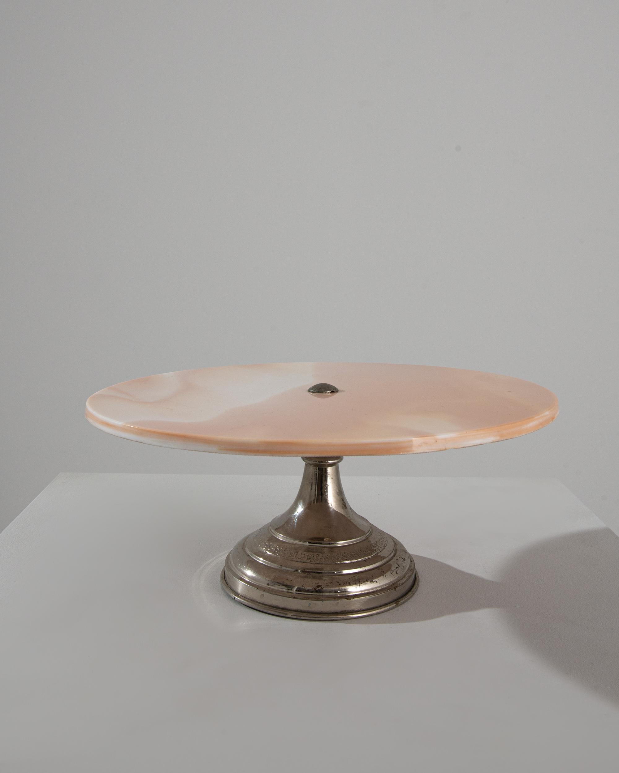 Dreamy and whimsical, this vintage cake tray is a delicious confection. Made in turn of the century Belgium, the design achieves a perfect balance of elegance and clarity: a simple circle of marble sits atop a silver-plated base. A raised motif of