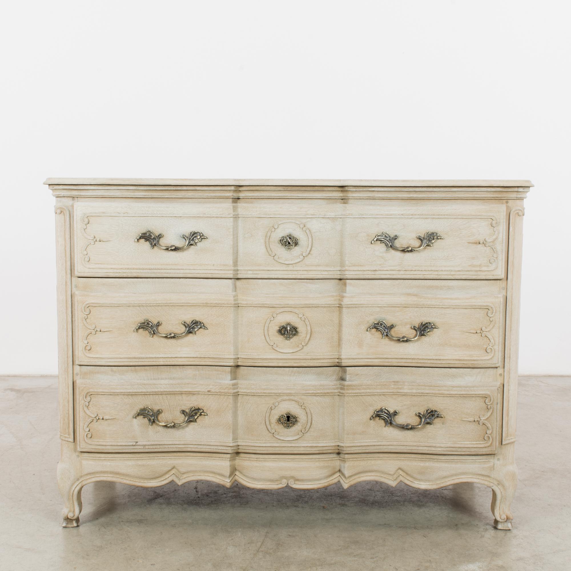 An oak chest of drawers from Belgium, circa 1900. A rococo shape with three serpentine drawers, which pull out with gilded filigree handles. Cabriole feet with dainty hooves elevate the cabinet; an undulating apron mimics the curves of the case. The