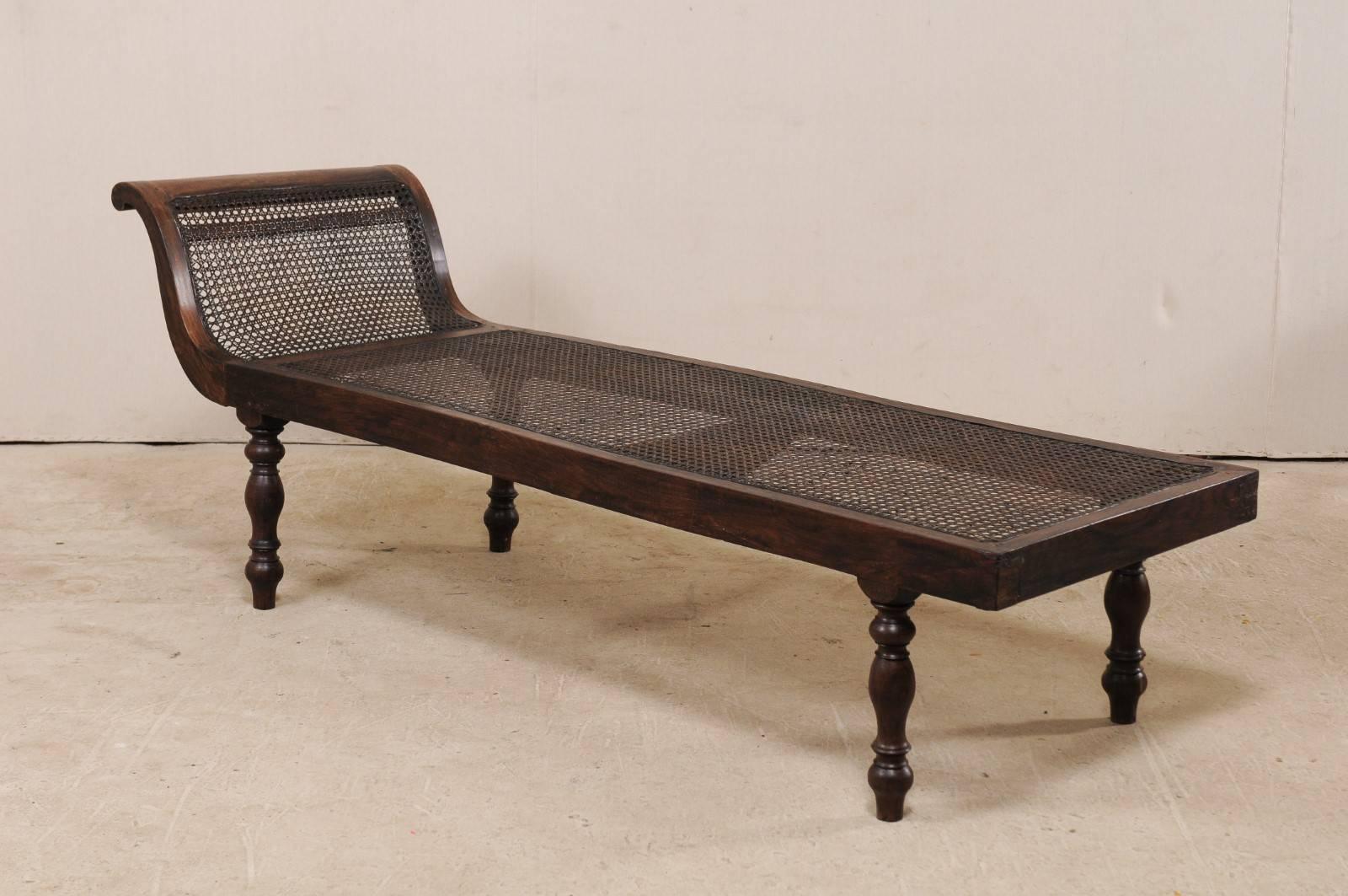 A British Colonial caned chaise longue from the turn of the 19th and 20th century. This antique Anglo-Indian tropical chaise is long and sleek, having just the right amount of carved detail, it features a graceful flowing form with hand caning from