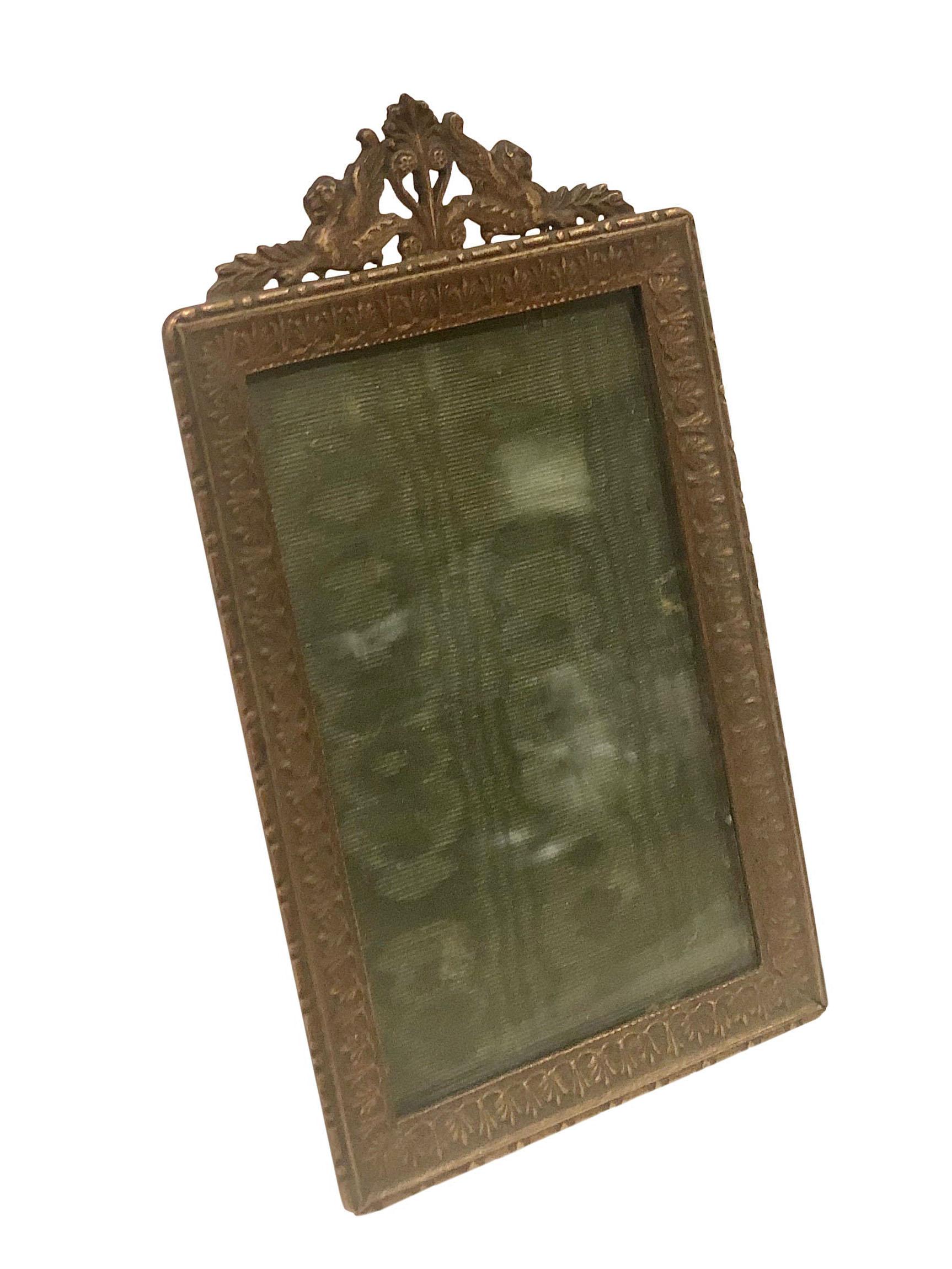 A bronze empire style small picture frame is from the turn of the century. The precious frame still has its original silk moire fabric inside from when it was sold.