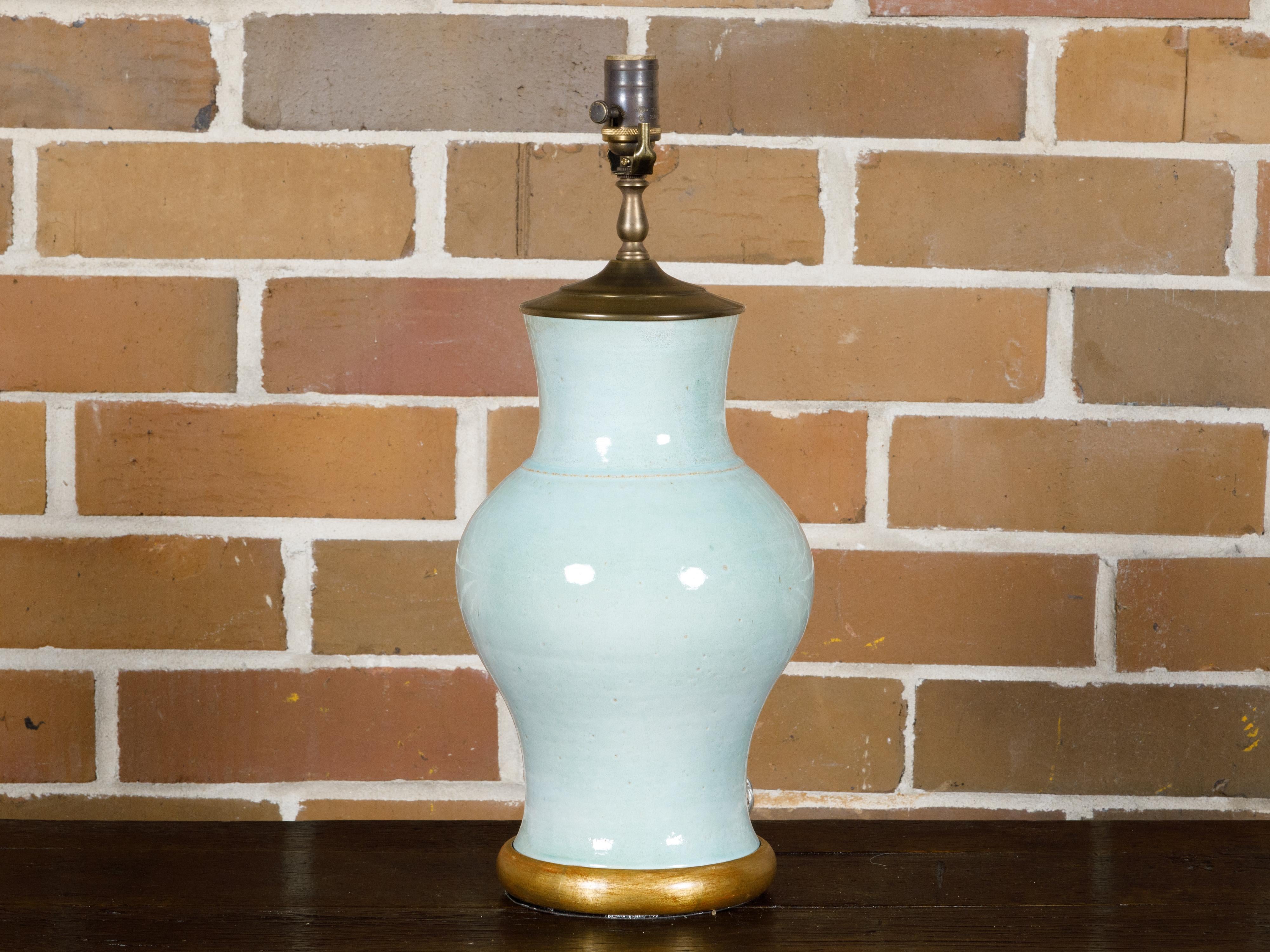 A Turn of the Century celadon table lamp from circa 1900 with gilded wood circular base. This exquisite Turn of the Century table lamp, dating back to circa 1900, is a beautiful testament to timeless design. The lamp's body is crafted in a soft