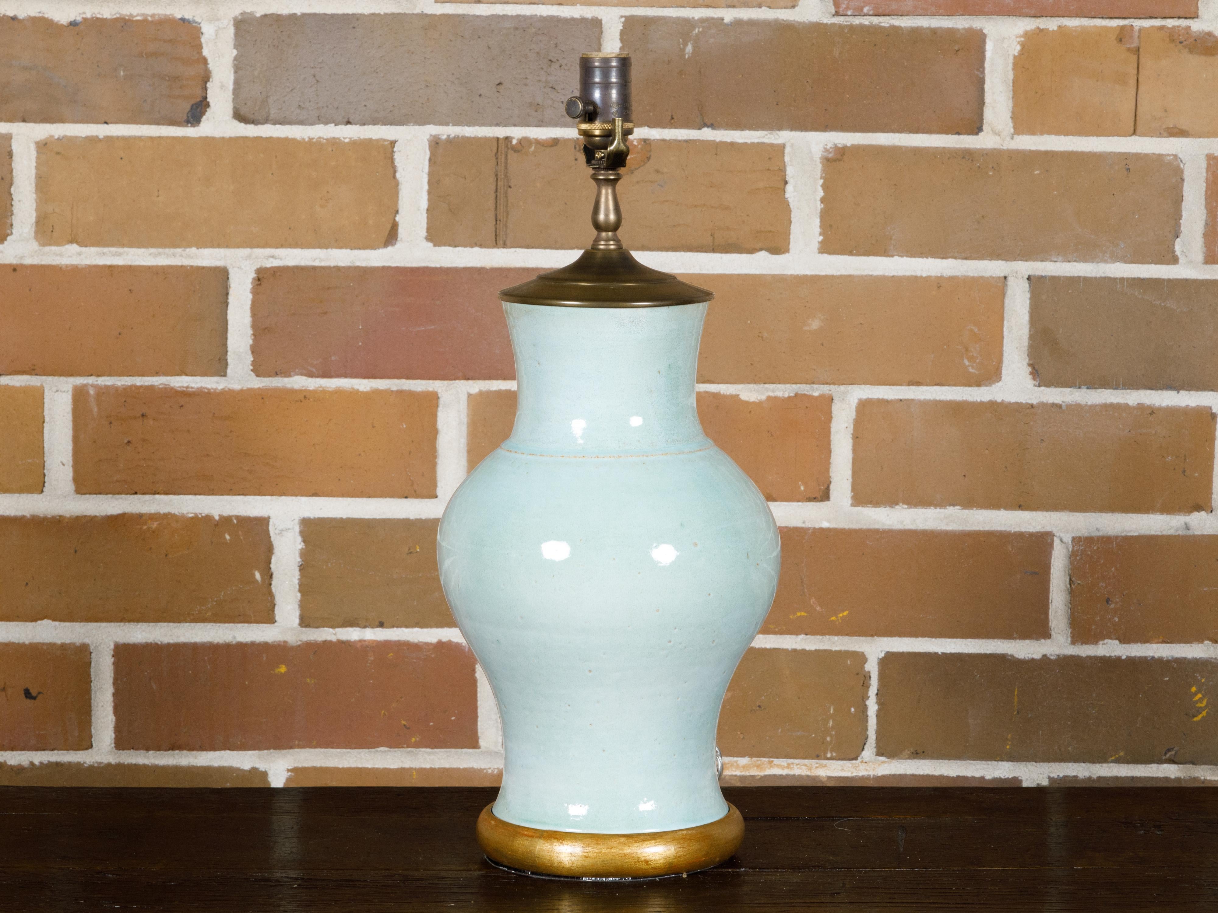 A celadon table lamp with gilded wood circular base. This exquisite table lamp is a beautiful testament to timeless design. The lamp's body is crafted in a soft celadon hue, evoking a sense of calm and elegance that is both subtle and striking.