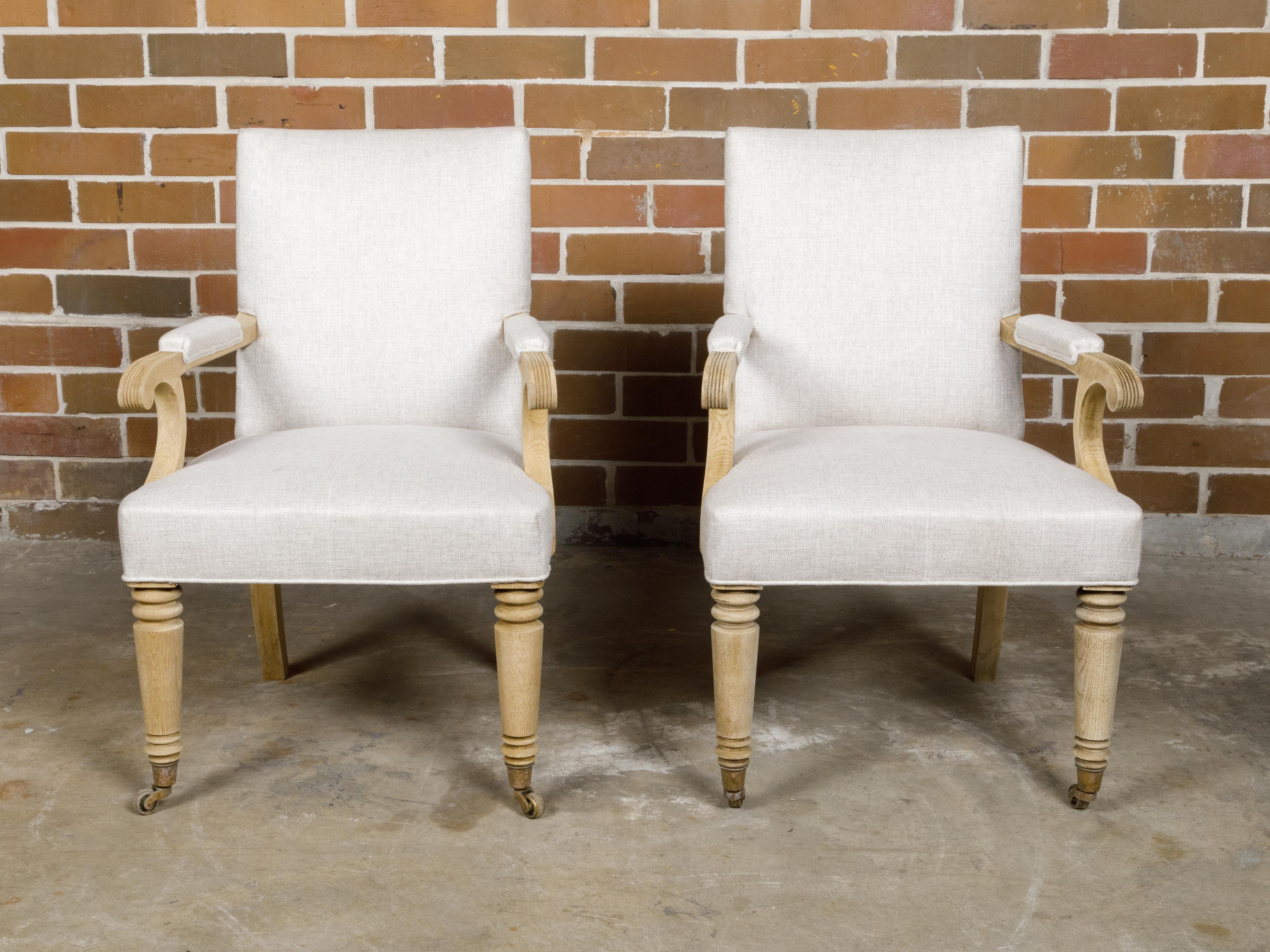 A pair of English Turn of the Century bleached wood armchairs from circa 1900 with elegant arms, scrolling knuckles, turned legs in the front and saber legs in the back. Discover the understated elegance of these English Turn of the Century