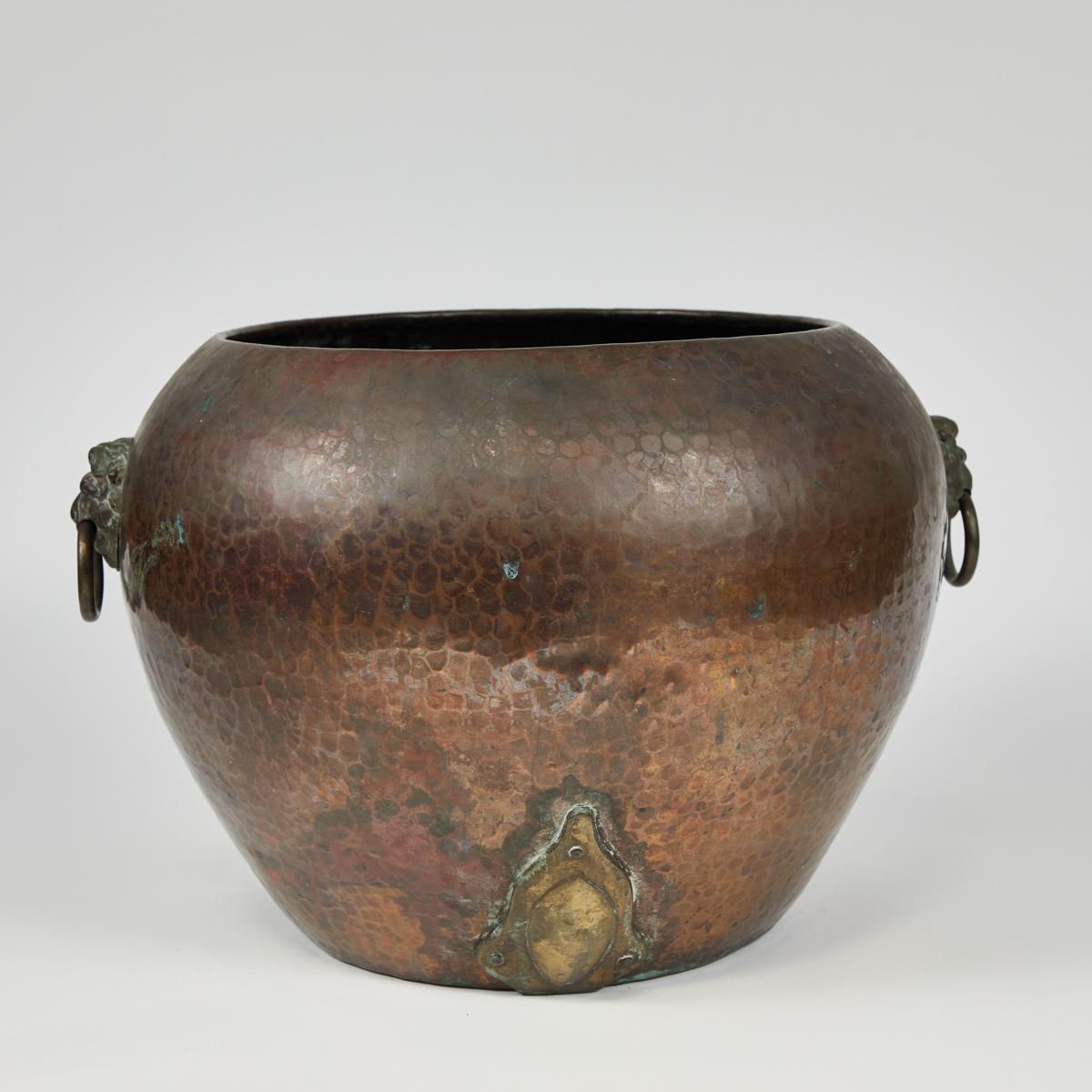 Medium-sized English Arts & Crafts copper hammered bucket or urn. The vessel features two metal lion sculptures, each holding a ring handle in its mouth. Sturdy, and with a wonderful deep patina, it would work well both indoors and outdoors.