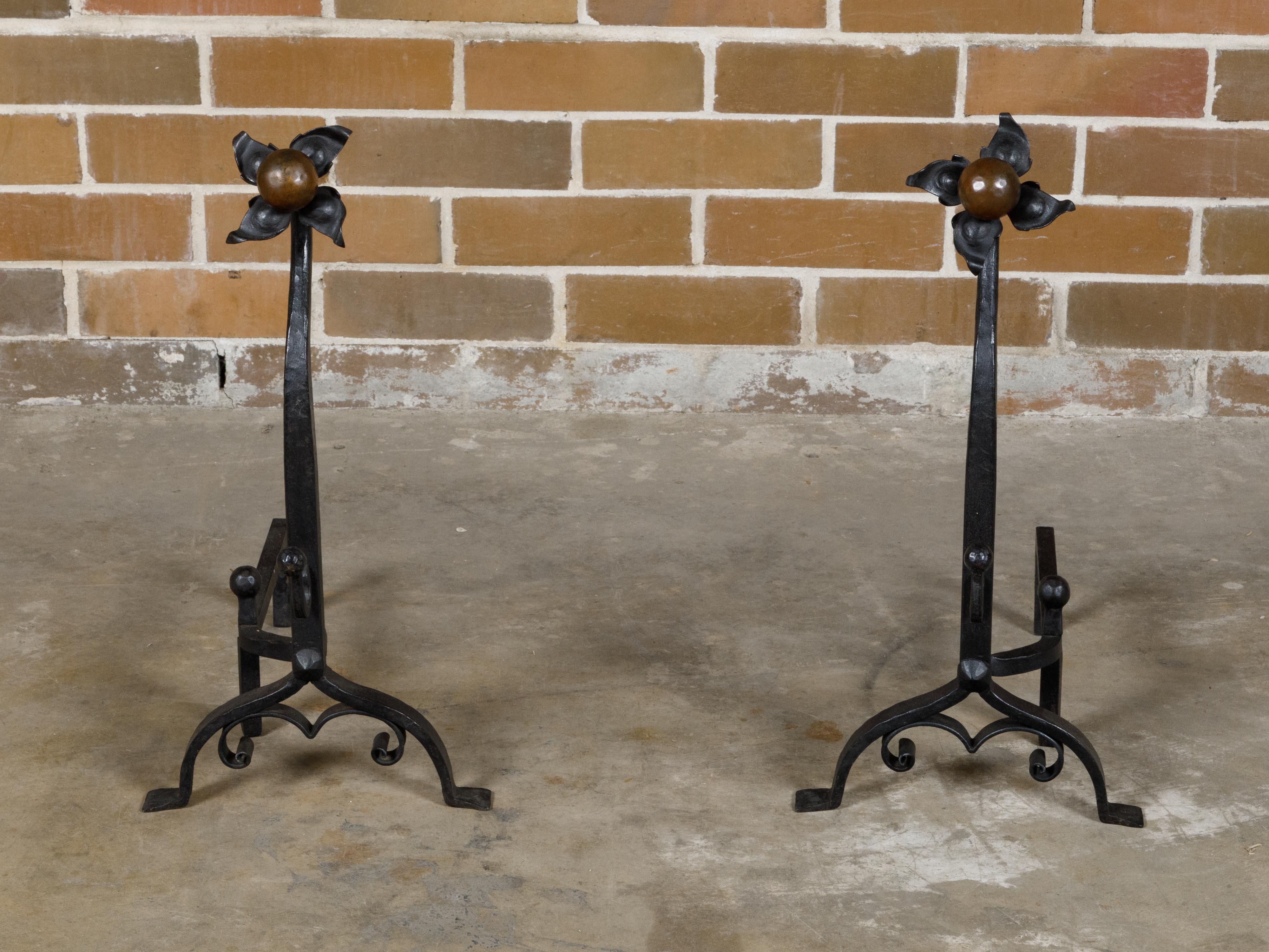 A pair of English Turn of the Century iron and copper andirons from circa 1900 with floral motifs. At the turn of the 20th century, a pair of English andirons emerged, masterfully crafted from iron and adorned with copper detailing, showcasing