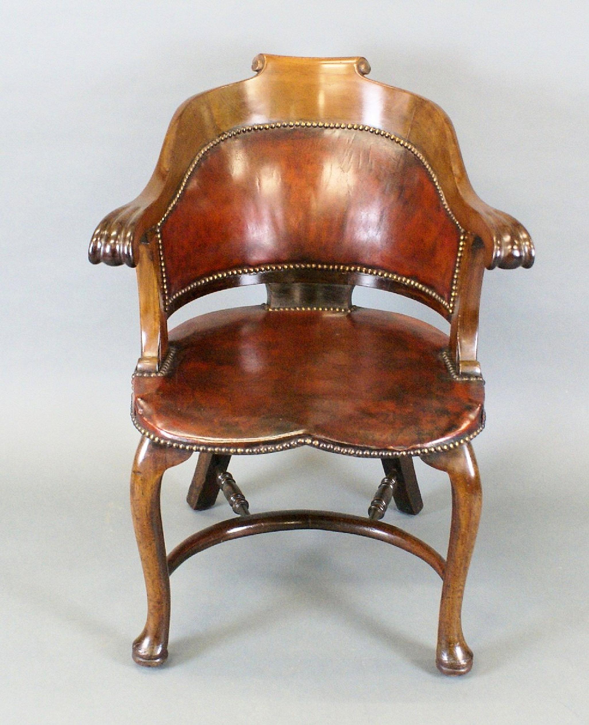This very handsome and well made English turn of the century armchair is made up of Walnut and a rich cognac brown leather upholstery. It features a shaped, curved back with scrolled arms. It is raised on cabriole front and swept back legs 
united