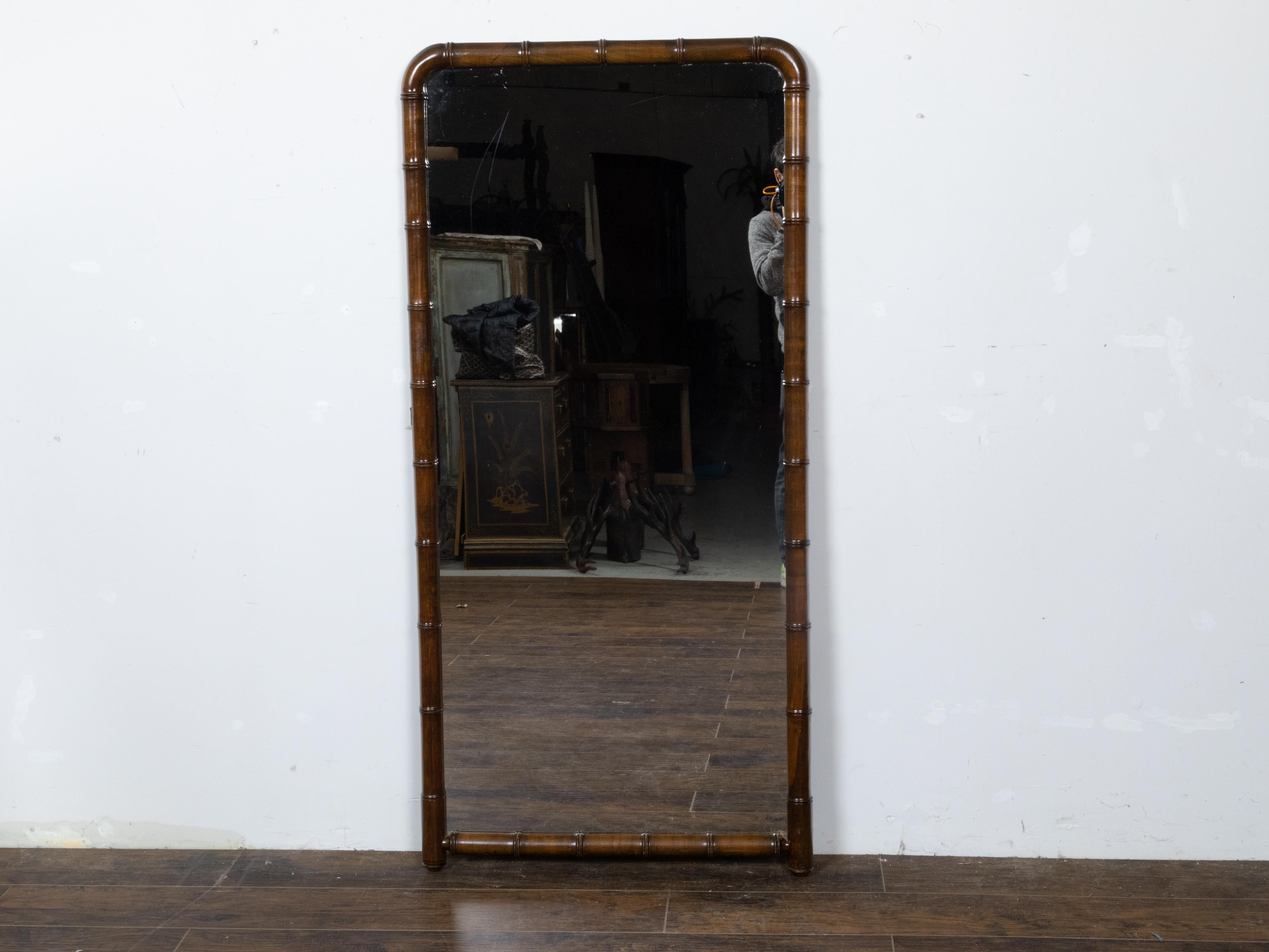 A Turn of the Century French faux bamboo walnut full length mirror from circa 1900 with rounded corners at the top and dark brown patina. Immerse yourself in the elegance and historic charm of this Turn of the Century French faux bamboo walnut