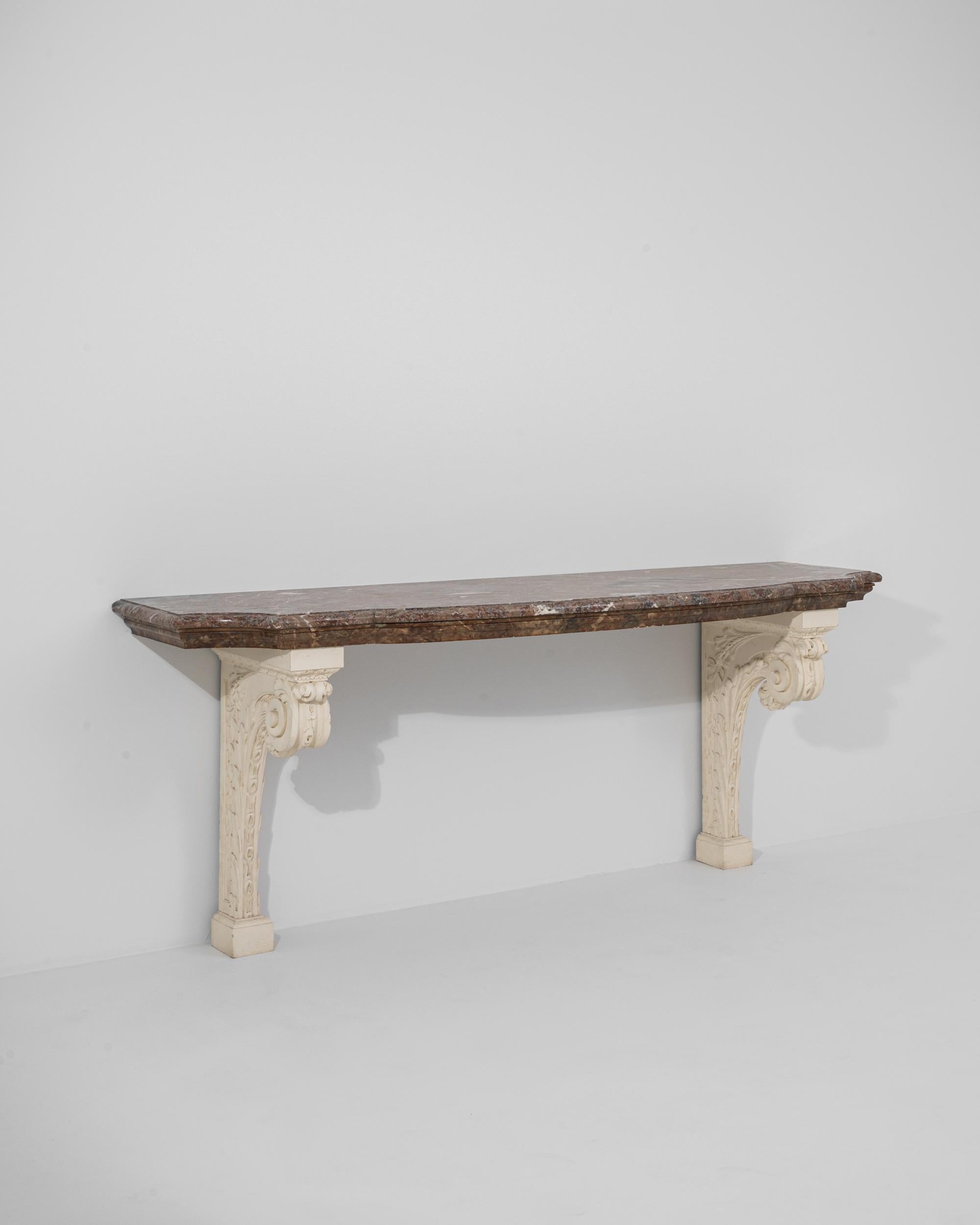 Luxurious and ornate, this turn of the century console table evokes the majesty of Baroque palaces and villas. Sourced from France, a contoured marble tabletop rests atop a pair of wooden brackets. The carved scrolls and leafy motifs of the