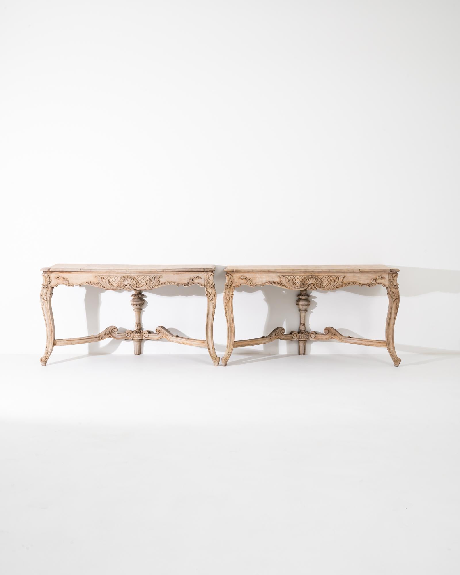 This pair of vintage console tables offer an elaborate Baroque design in natural oak. Made in France at the turn of the century, the design takes inspiration from the furniture of the royal courts of previous centuries, intended to dazzle spectators