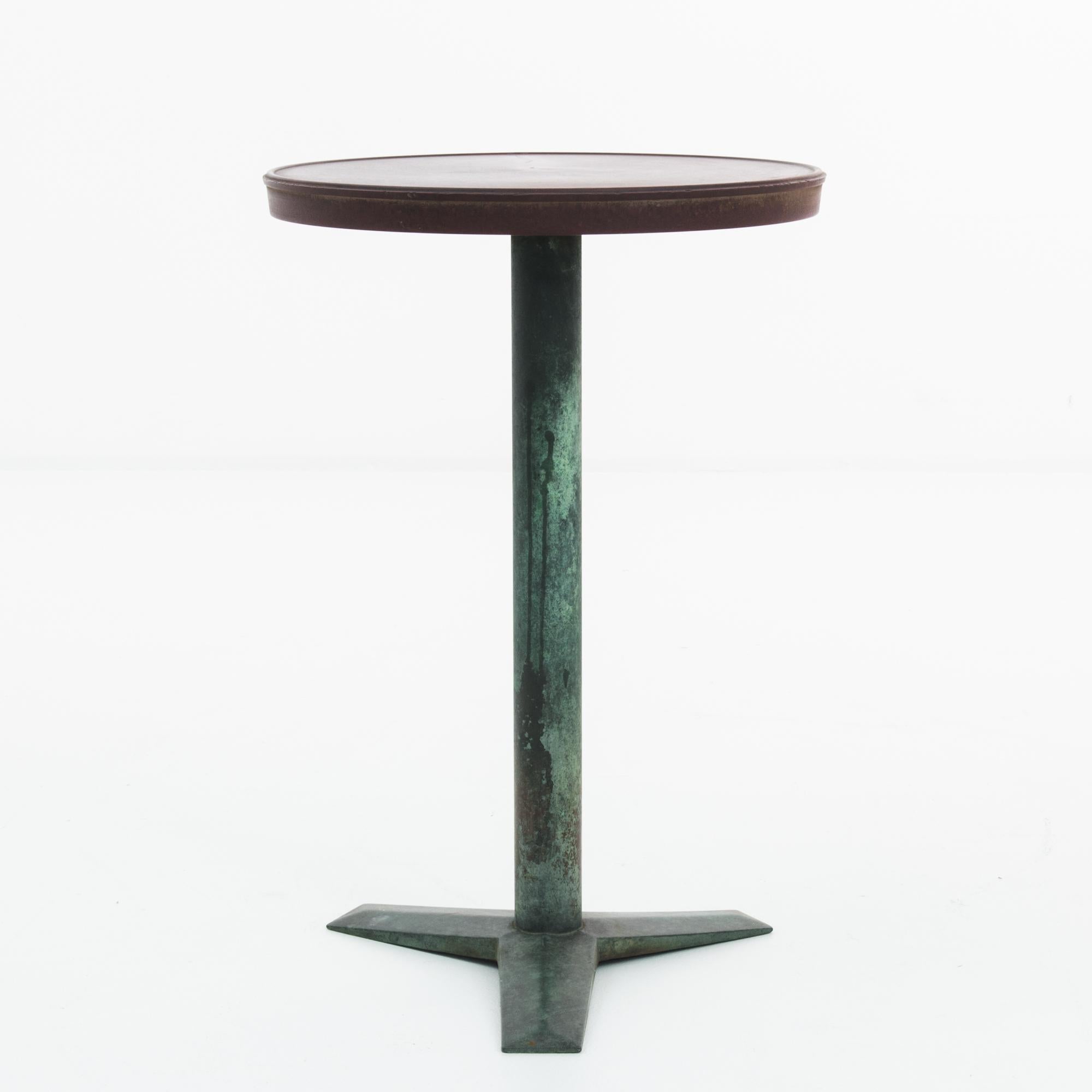 A brass side table from turn of the century France. The round tabletop sits atop a single column, creating a minimalist bistro silhouette. The burgundy tone of the tabletop makes a harmonious contrast with a beautiful verdigris copper patina,